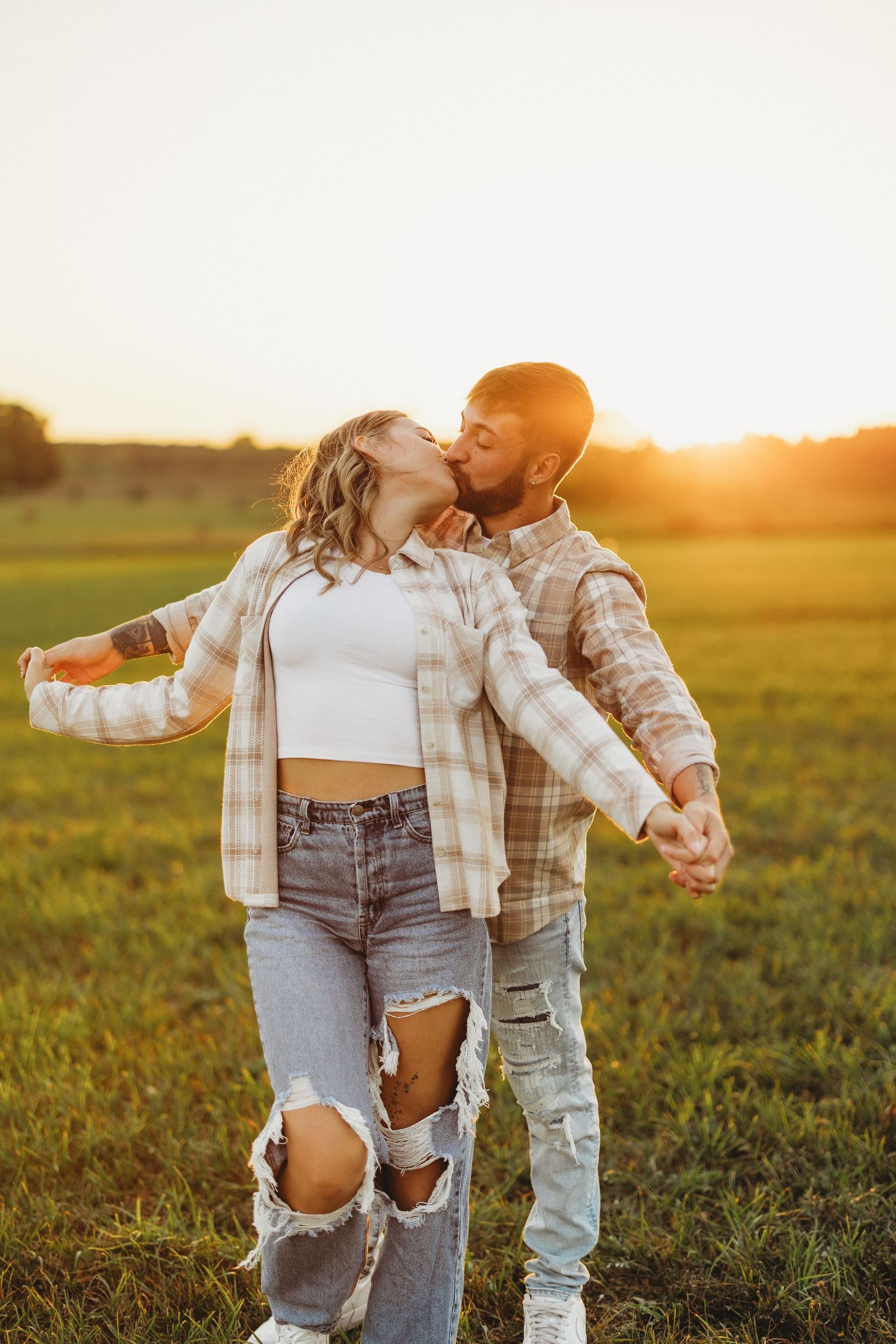 A couple in distressed denim and plaid sharing a joyful moment at sunset.