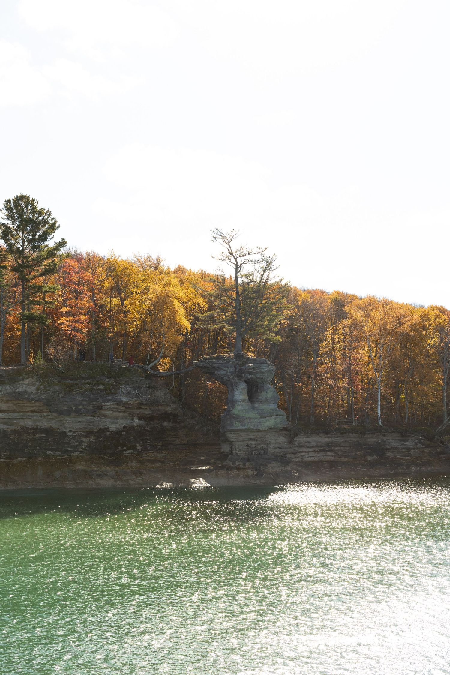 Limestone cliffs with autumn foliage reflecting in turquoise lake waters.