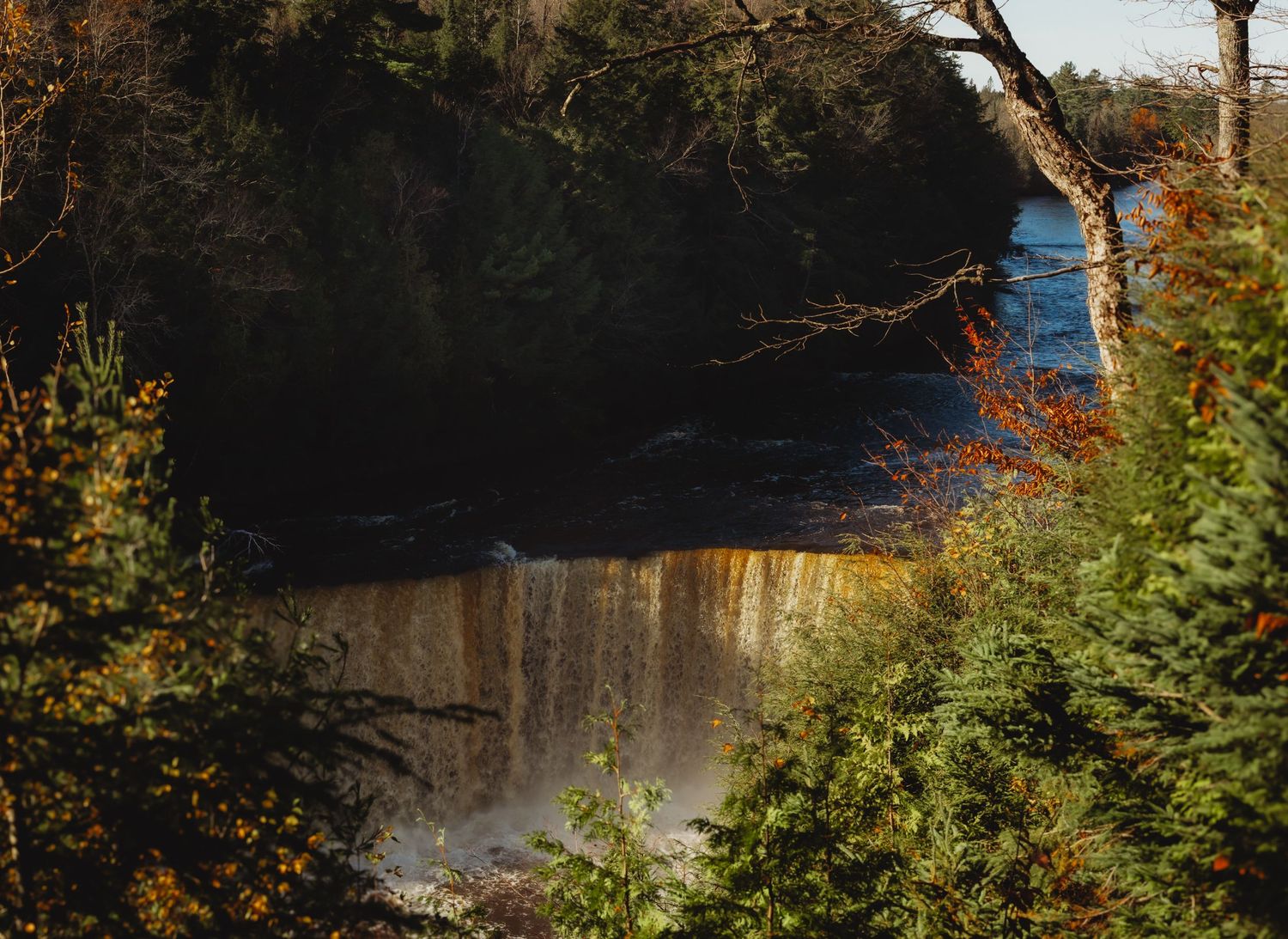 Wide waterfall cascading over multiple rock tiers with autumn foliage visible in the background.