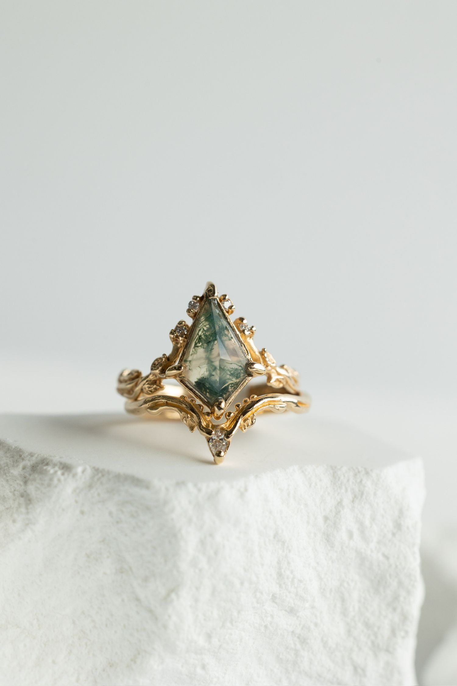 Gold ring with pale green gemstone in ornate setting displayed on white crystal formation.