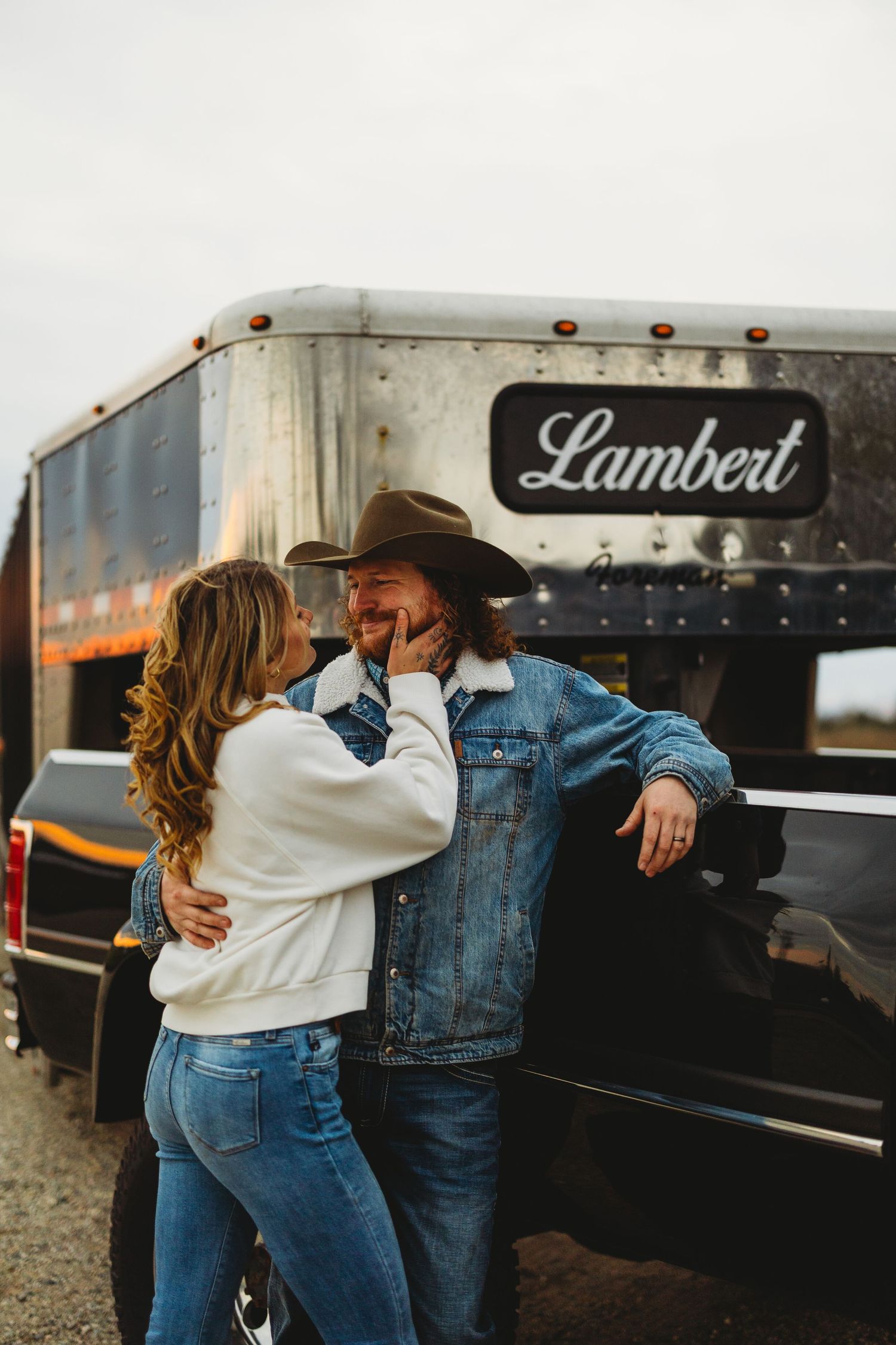 Couple embracing near a vintage Lambert trailer in casual denim outfits.