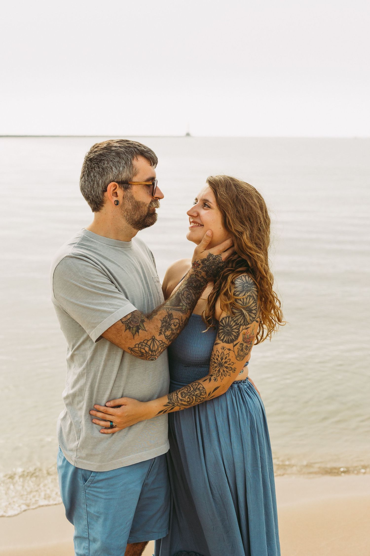 A couple shares tender moments in a series of romantic beach photos wearing coordinated blue and gray outfits.