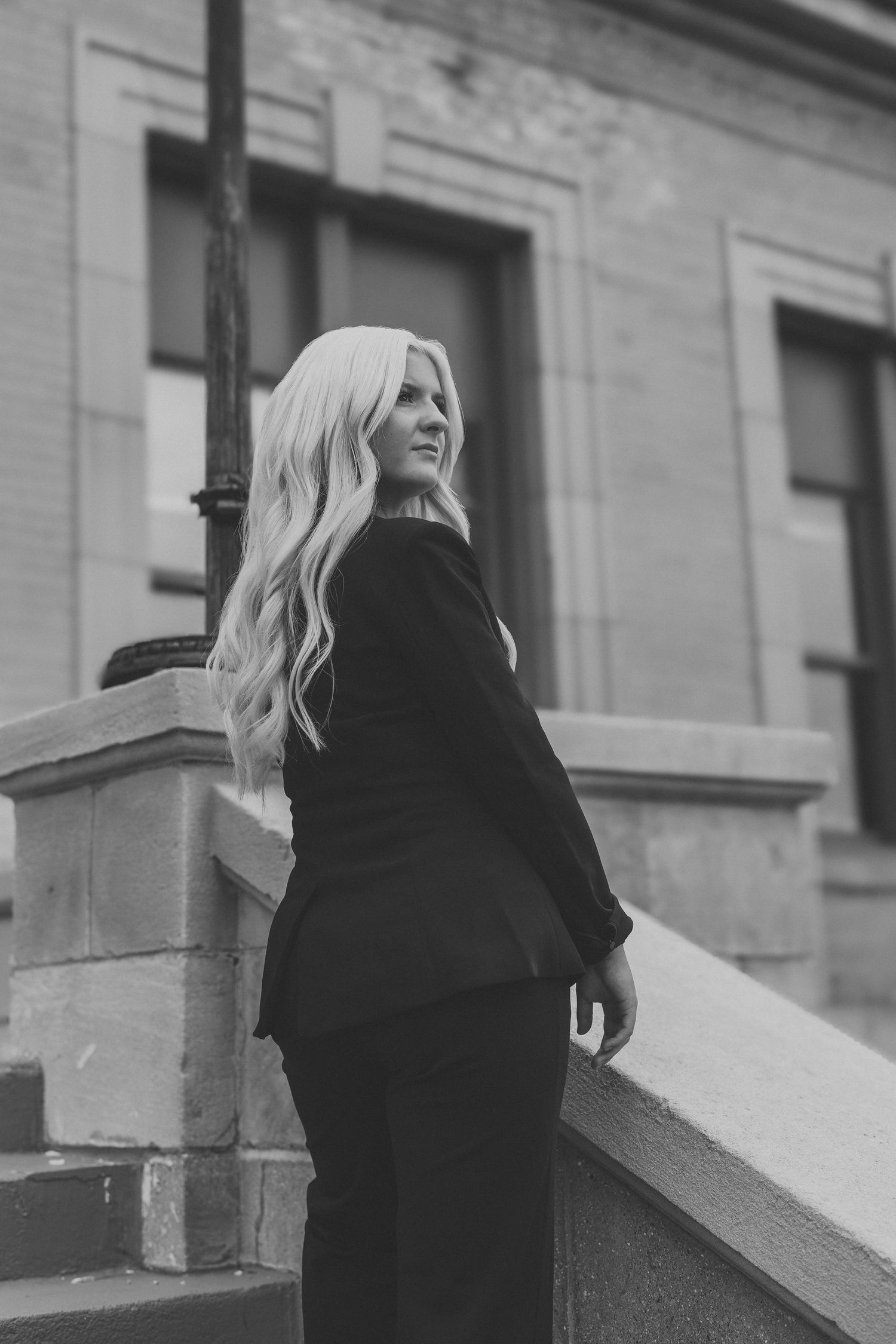 Black and white photo of a blonde woman in a black suit standing on steps outside a historic stone building.