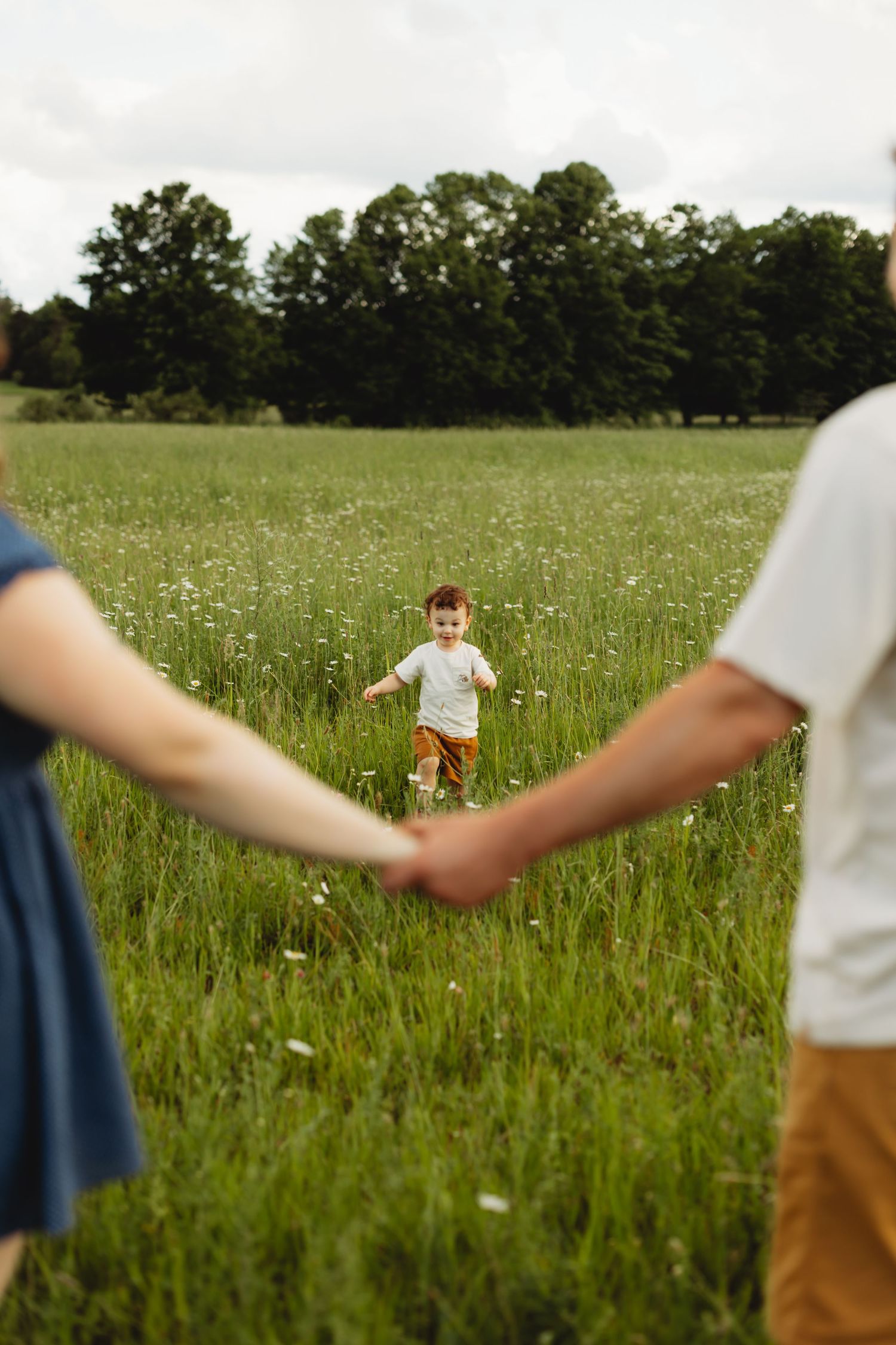 A joyful child runs through a green meadow toward two adults holding hands in the foreground.