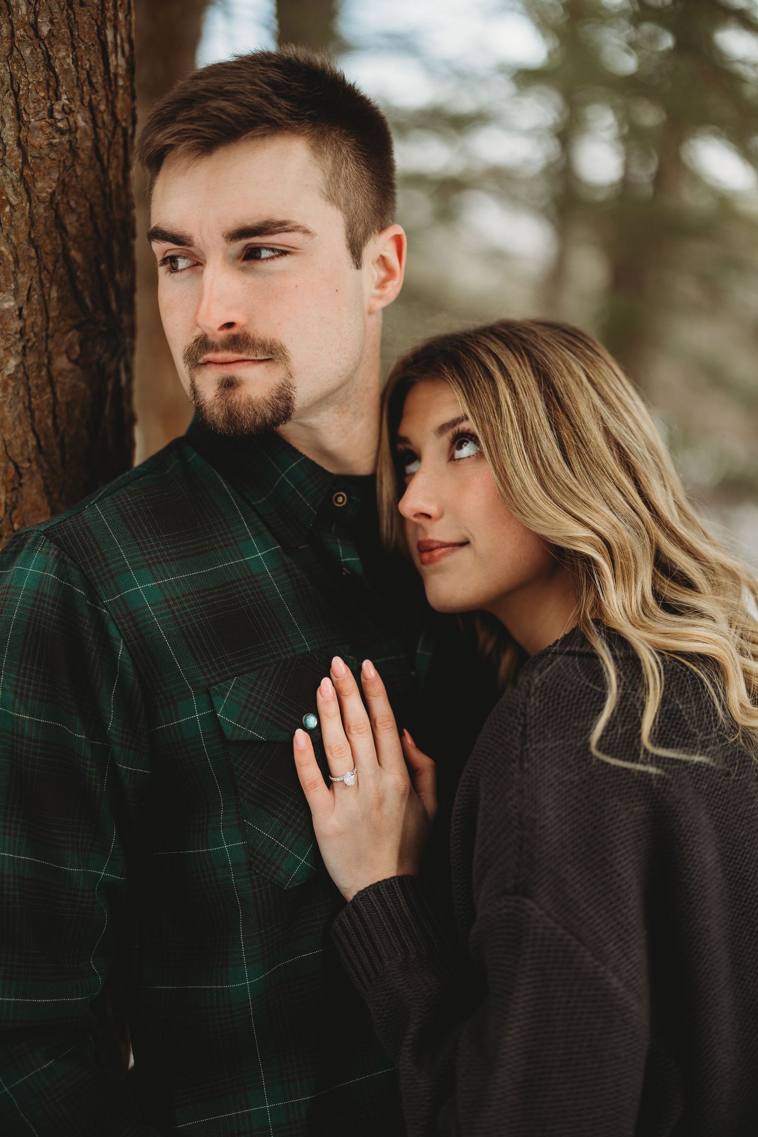 Romantic winter couple portraits against pine trees showing intimate moments.