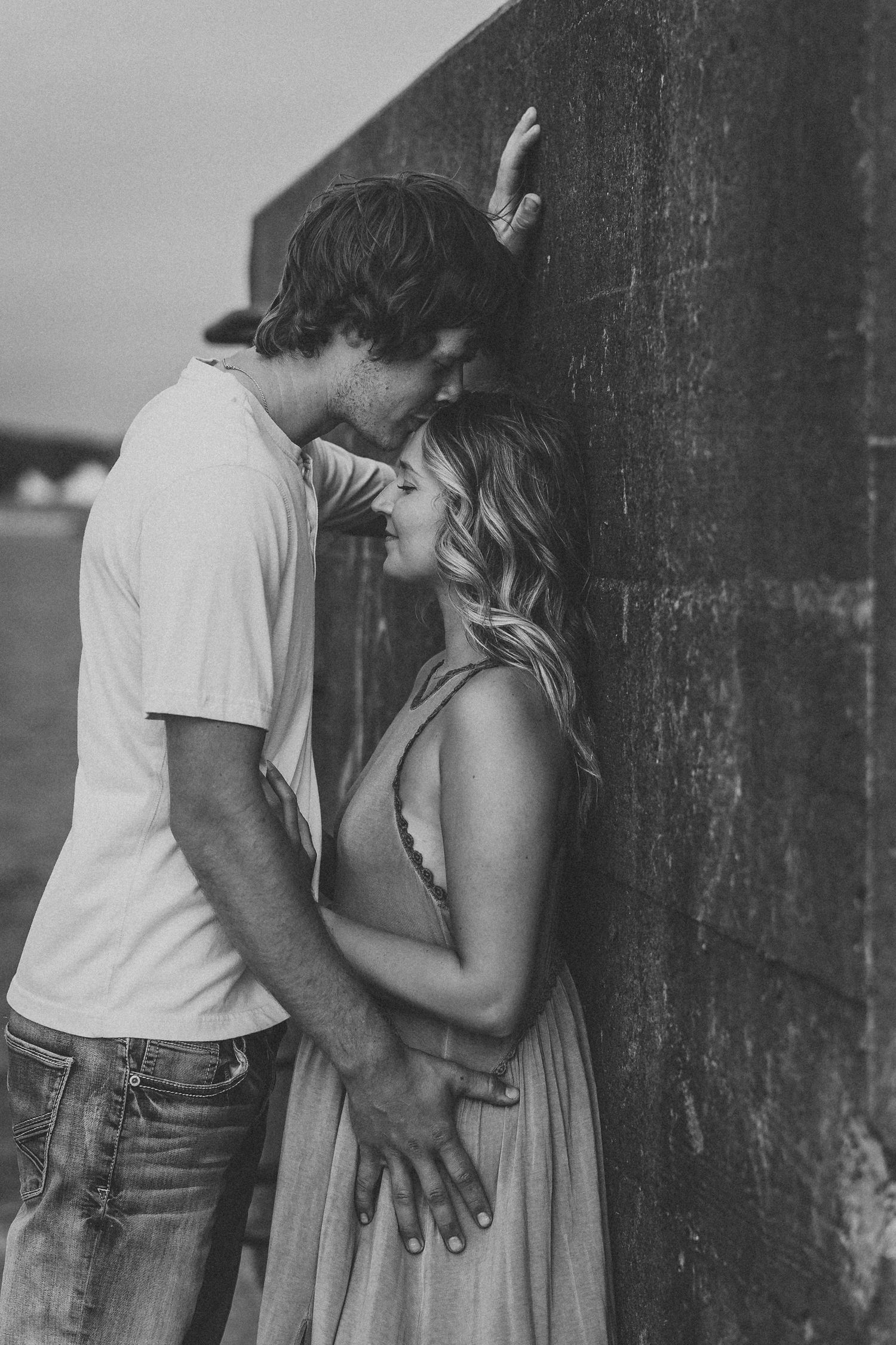 A romantic black and white photo series of a couple embracing against a textured wall.
