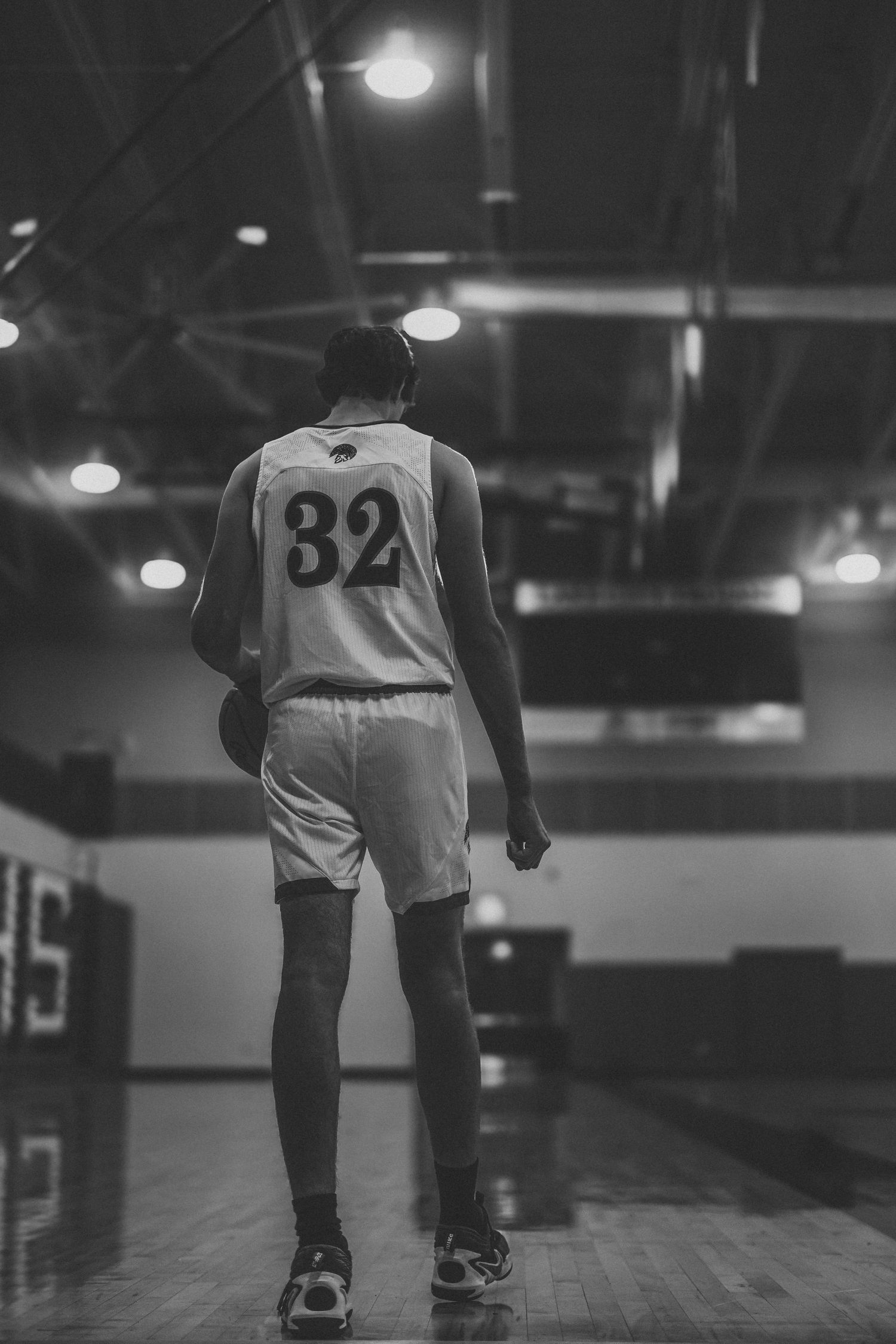 Basketball player in white jersey number 82 walks across dimly lit court.