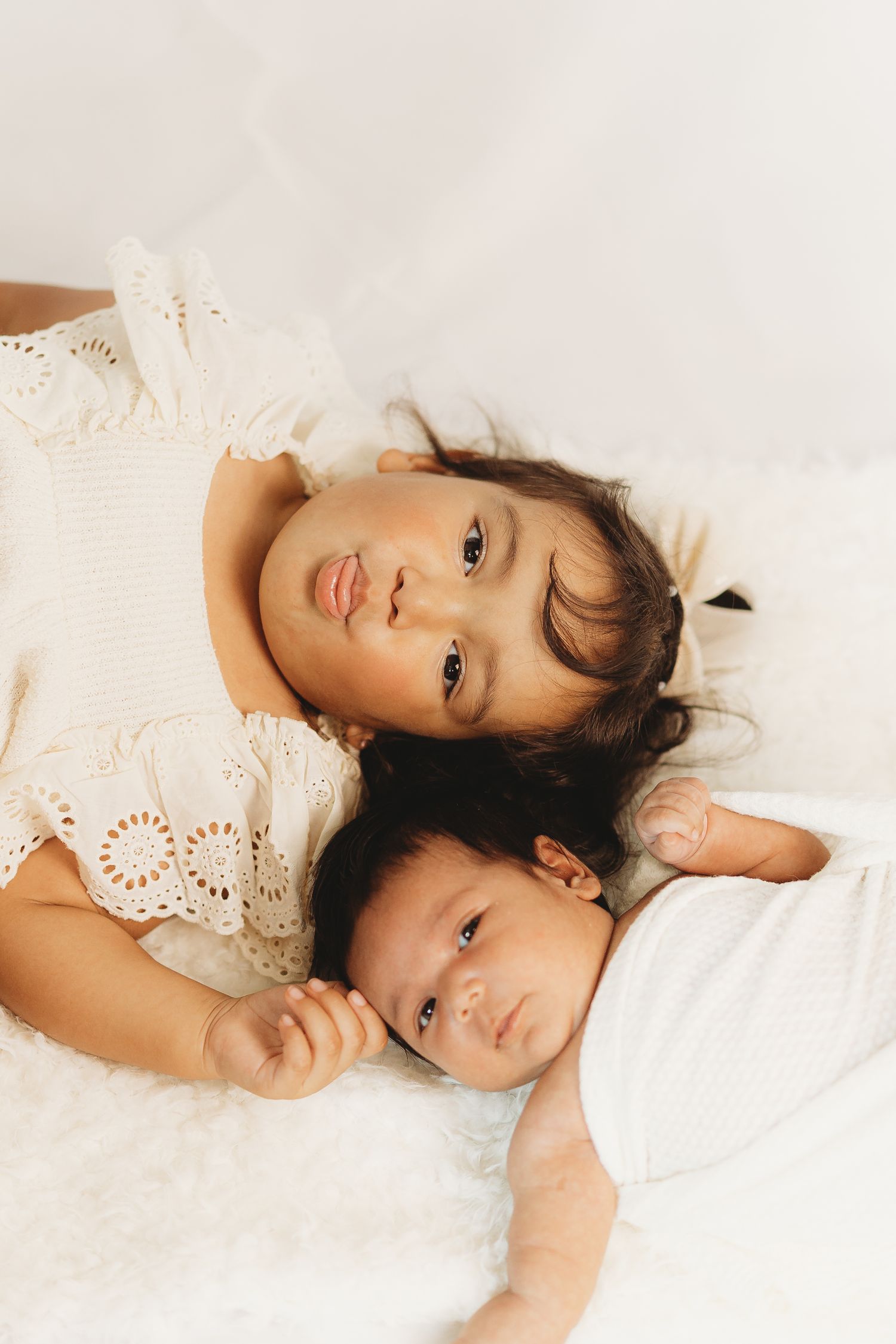 Siblings lying together on white bedding during intimate portrait session.
