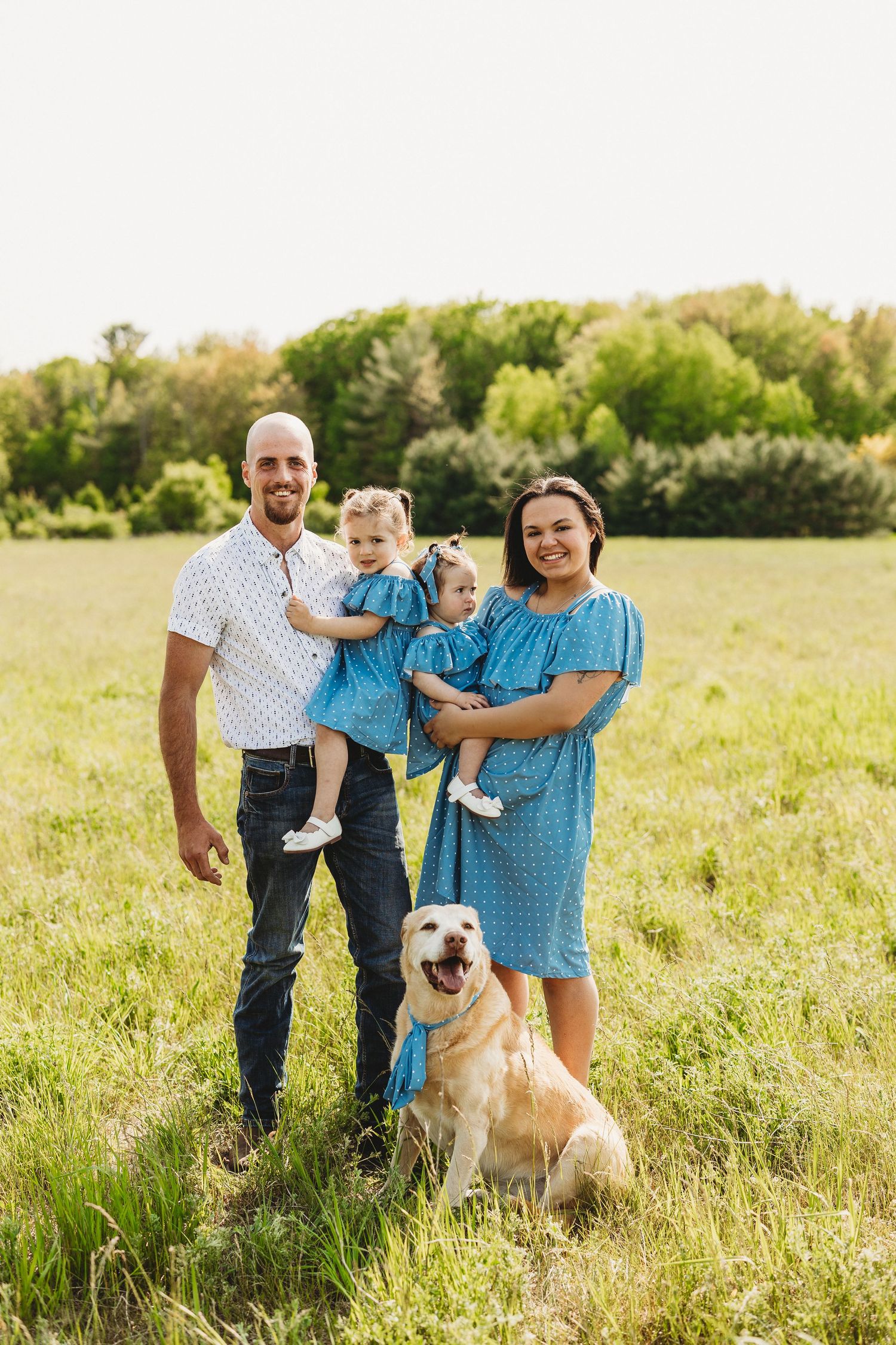 A family and their golden retriever dog pose together in a sunny meadow on a warm summer day.