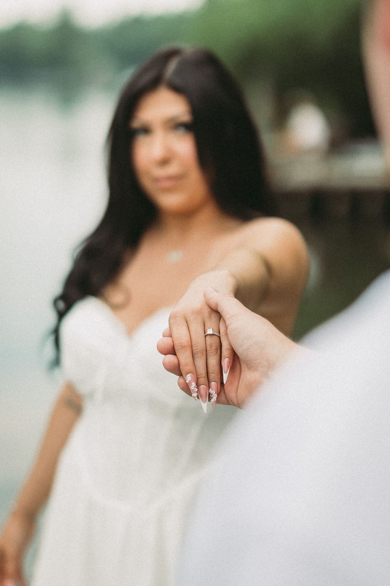 A person in a white dress poses outdoors showing off their engagement ring in a series of romantic photos.