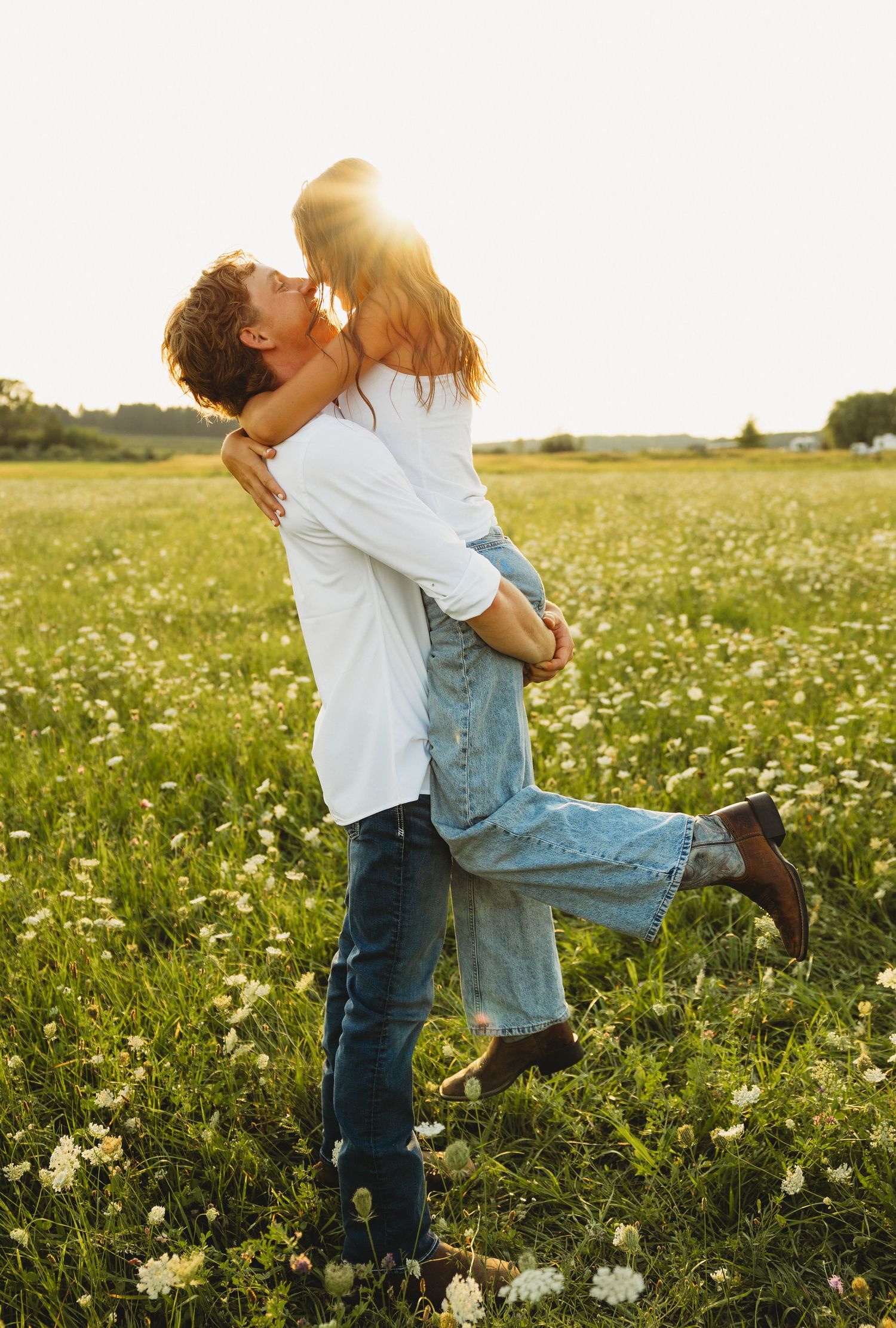 Man lifting woman in a romantic embrace in a sunny wildflower meadow at golden hour.
