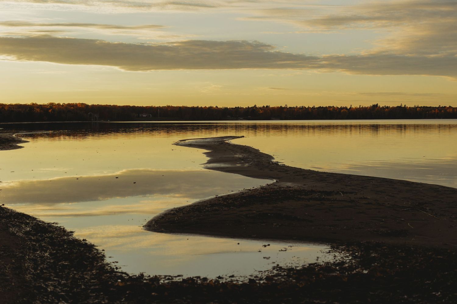Golden sunset illuminates a curved shoreline with dramatic cloud formations.