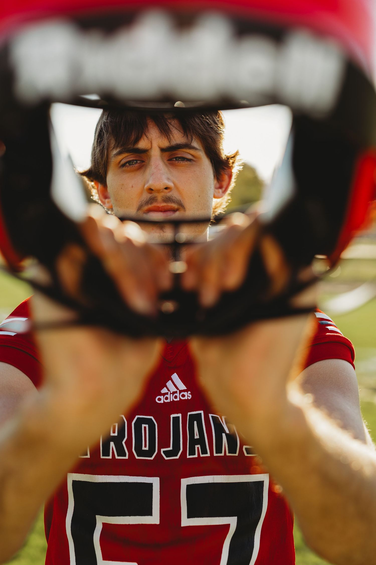 Creative reflection shot through football helmet visor showing player in red Trojans jersey.