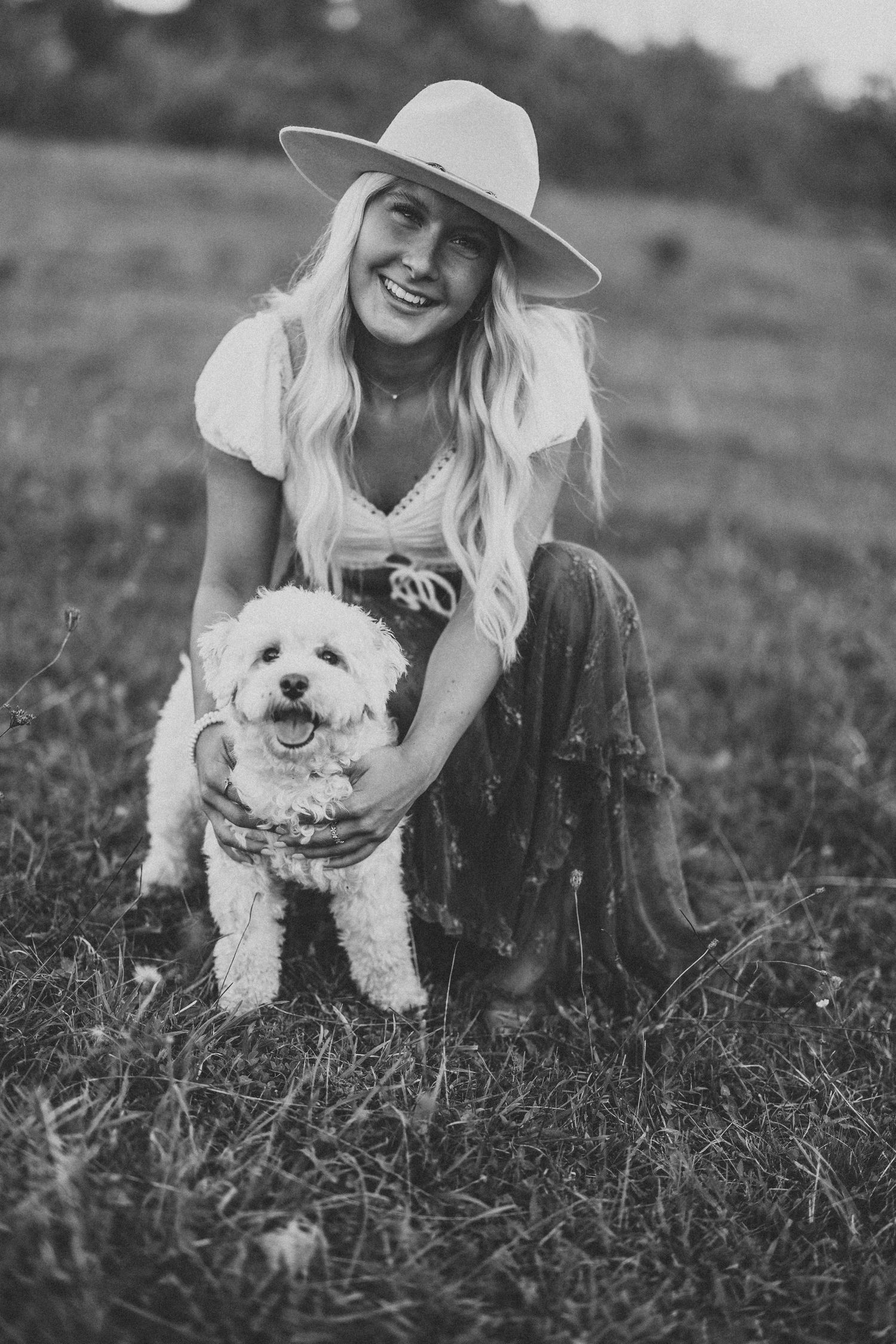 A white fluffy dog plays in a grassy field during a black and white photoshoot.