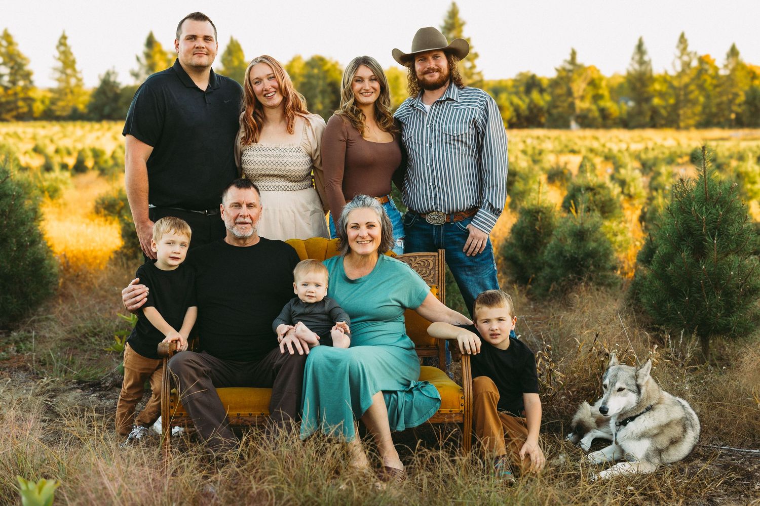 Extended family sitting together on yellow couch in field during sunset.