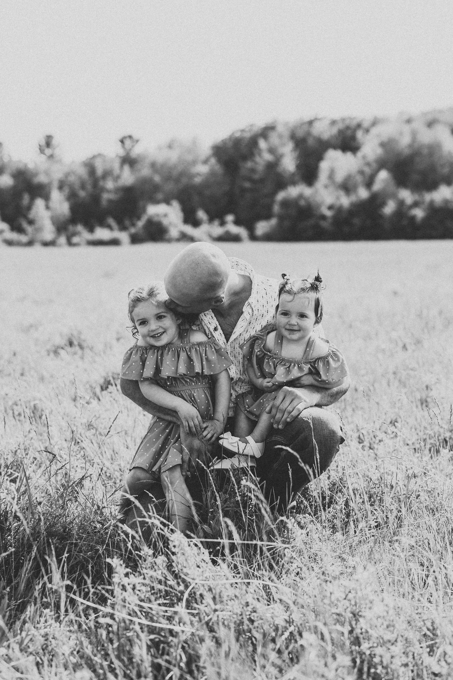 A black and white photograph shows children sitting together in a grassy field on a sunny day.