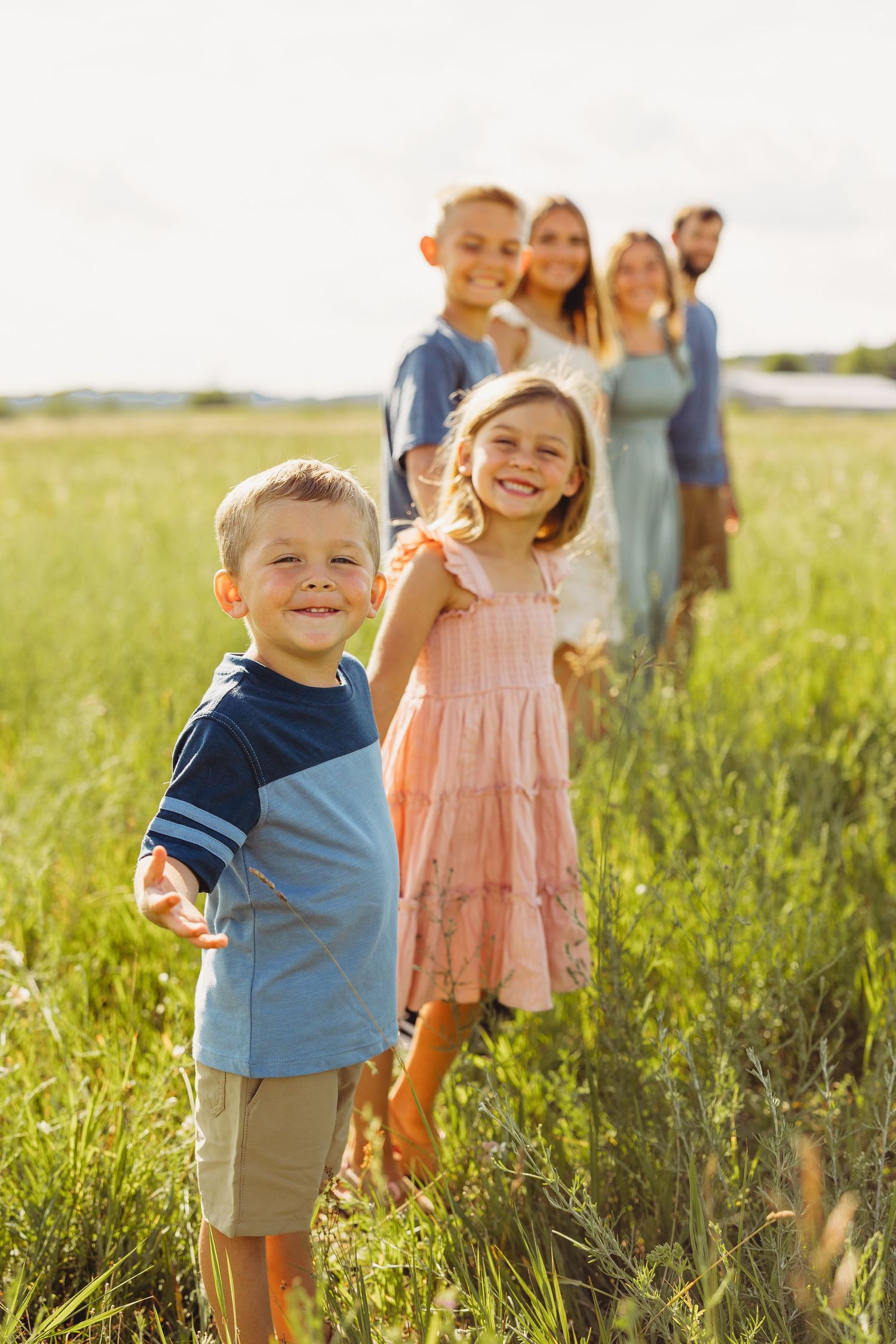 A joyful family with children smiling in a sunny green field, with parents standing together in the background.