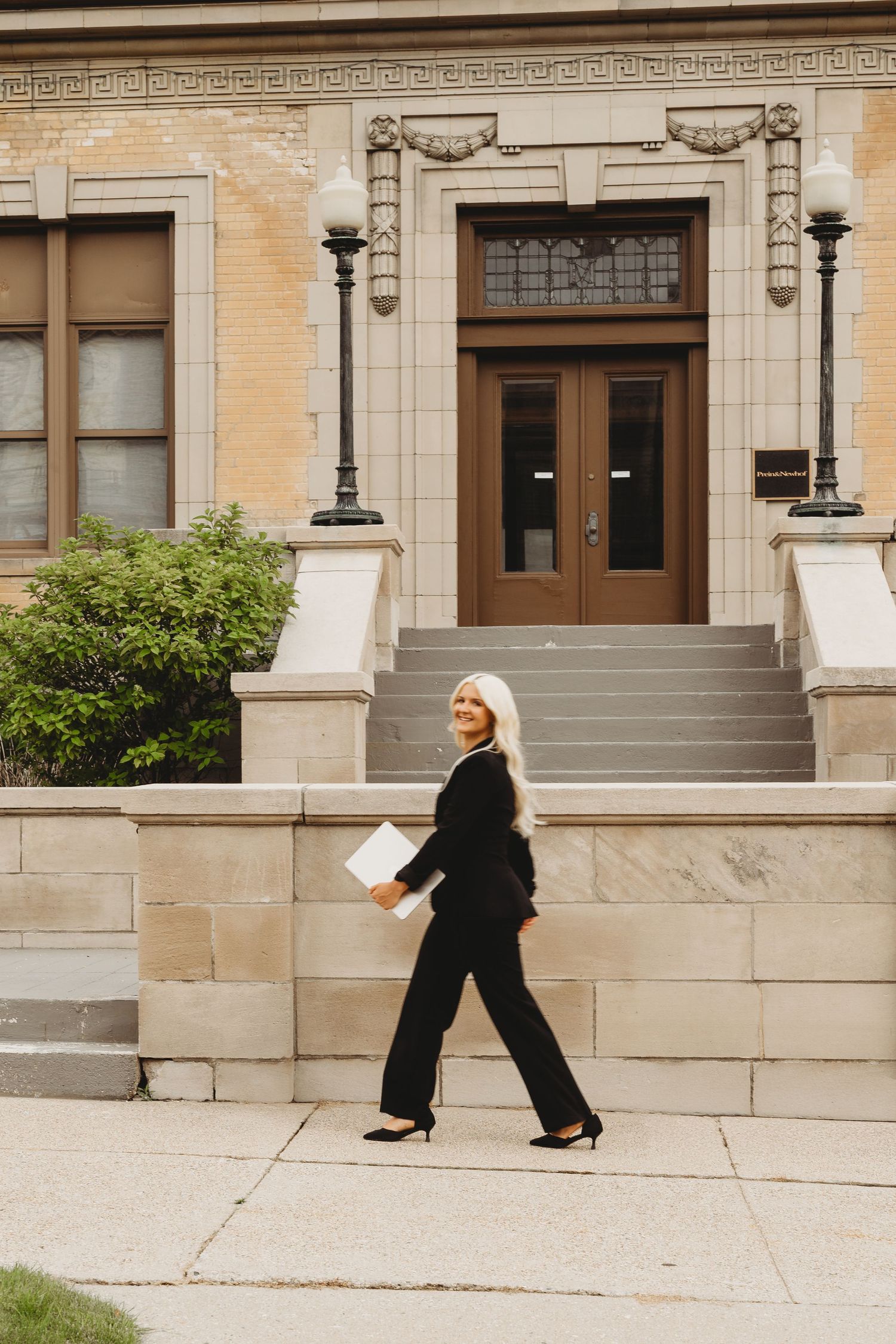 Professional woman in black suit walking confidently outside a classic stone building, carrying documents.
