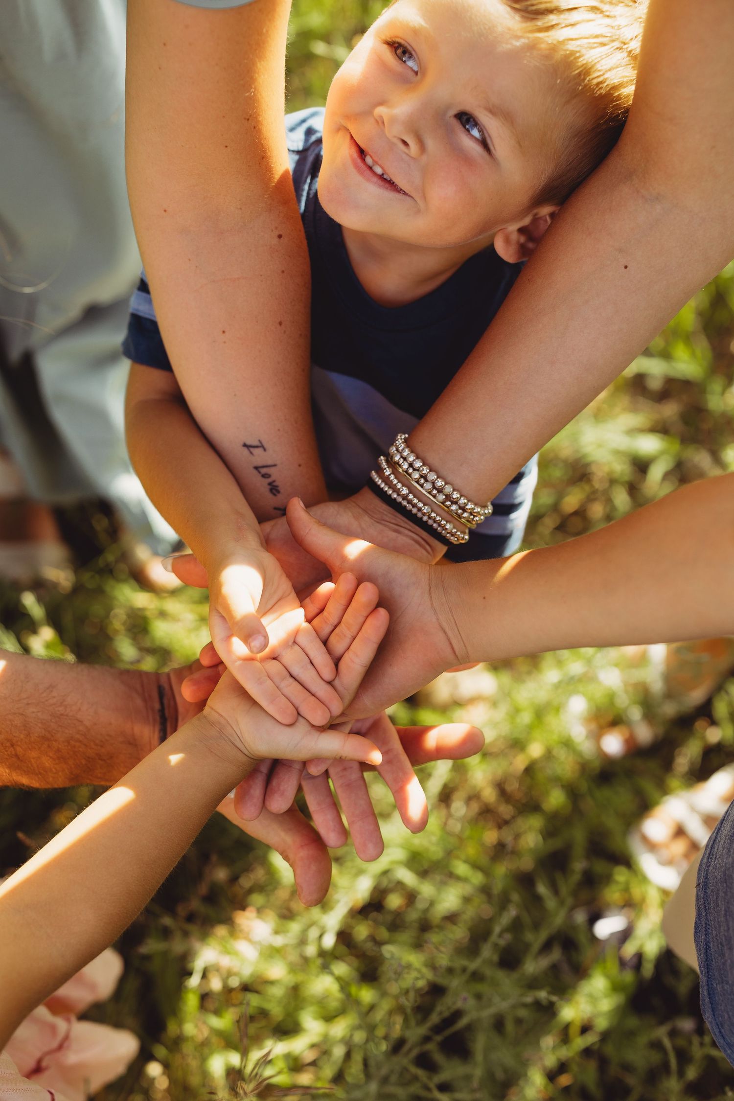Happy boy smiling as family stacks hands together outdoors in sunny green field, unity and togetherness concept.