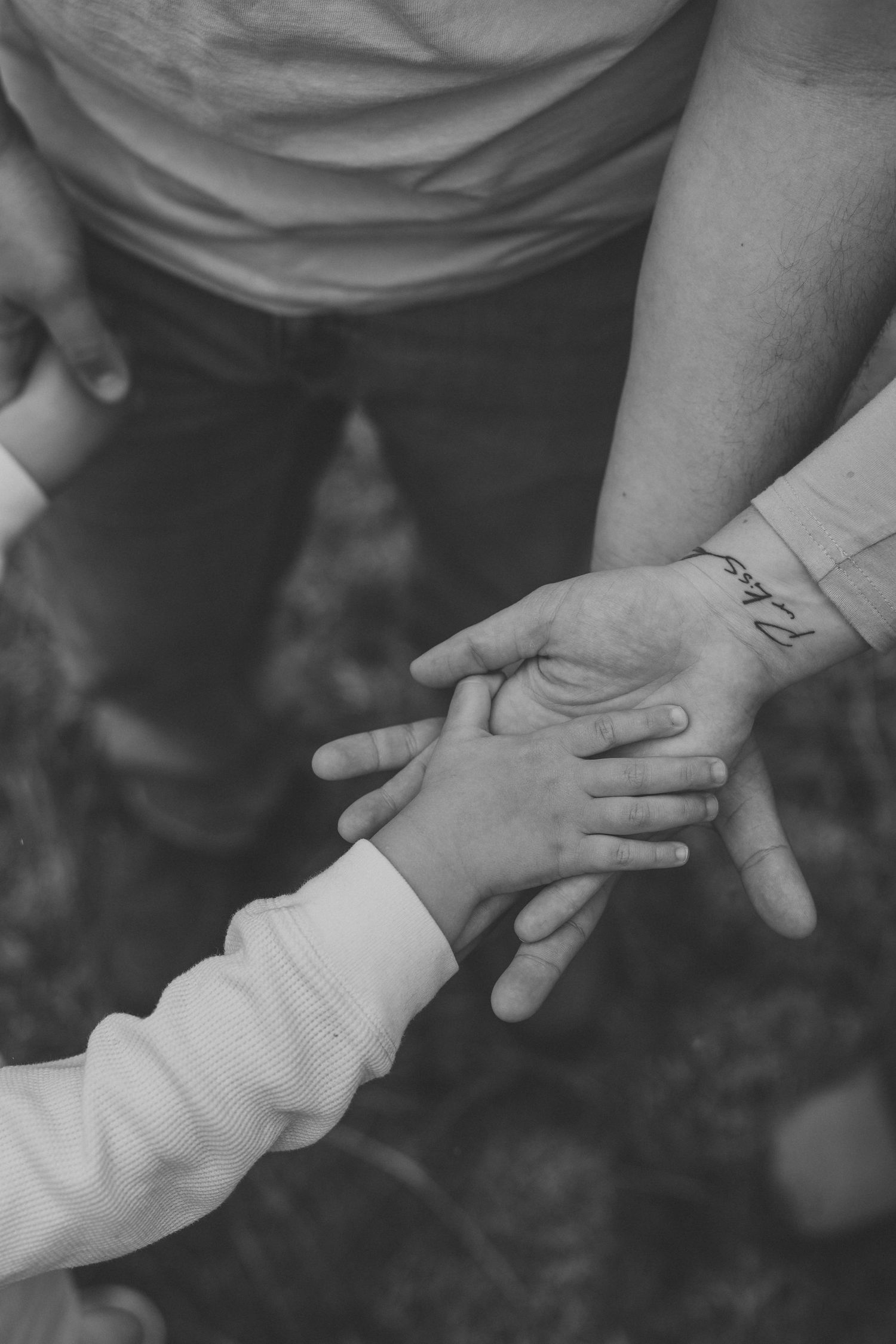 Black and white photo of an adult holding a small child's hand, showing a tender family moment with a wrist tattoo visible.