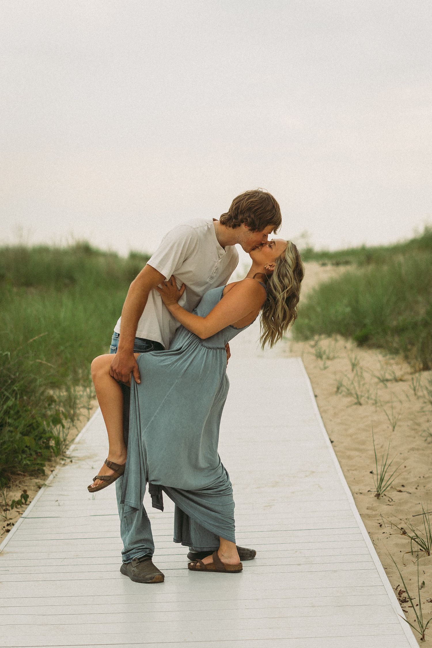 Romantic poses on a wooden boardwalk near beach dunes.