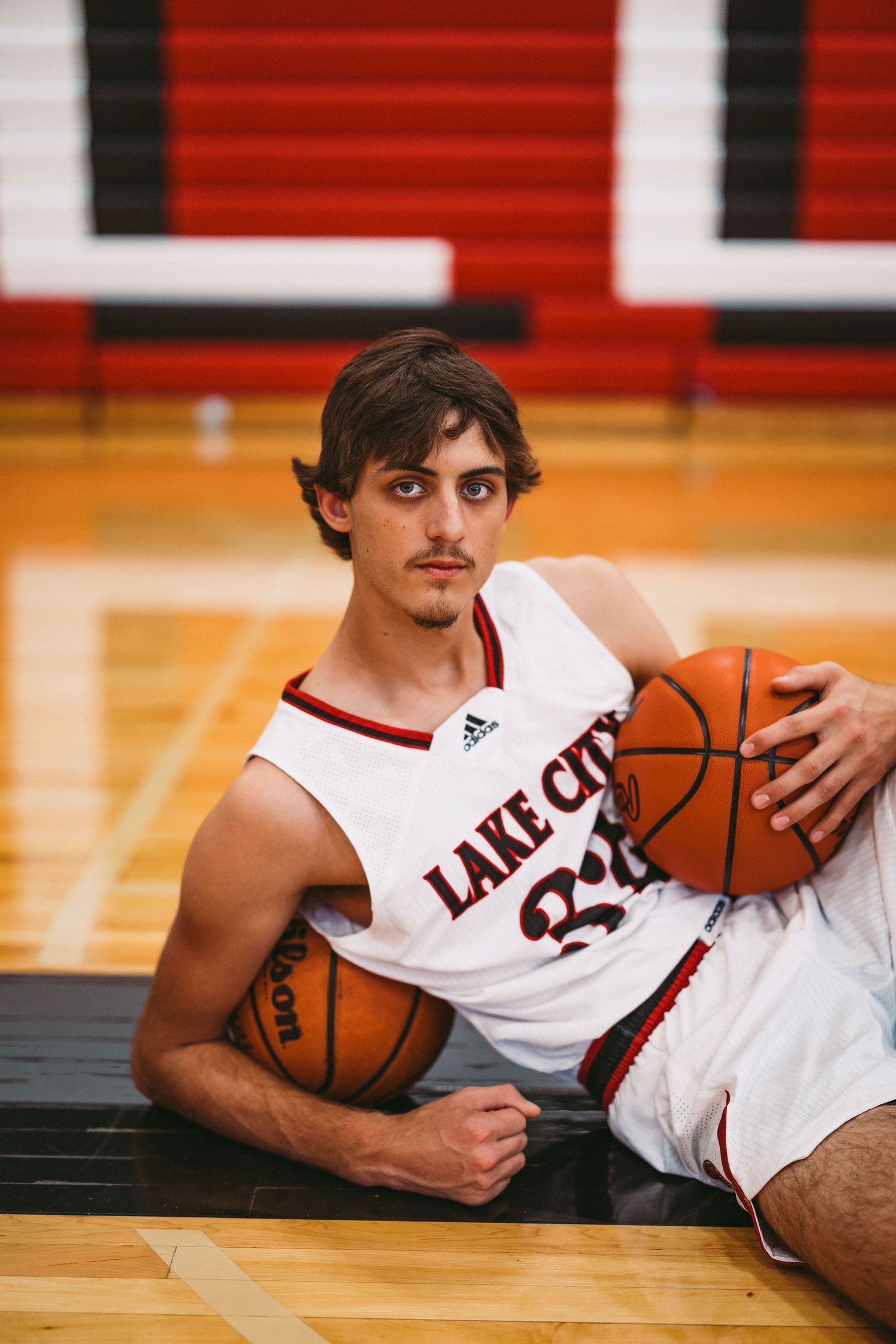 Basketball player in Lake City jersey poses with ball on gymnasium floor.