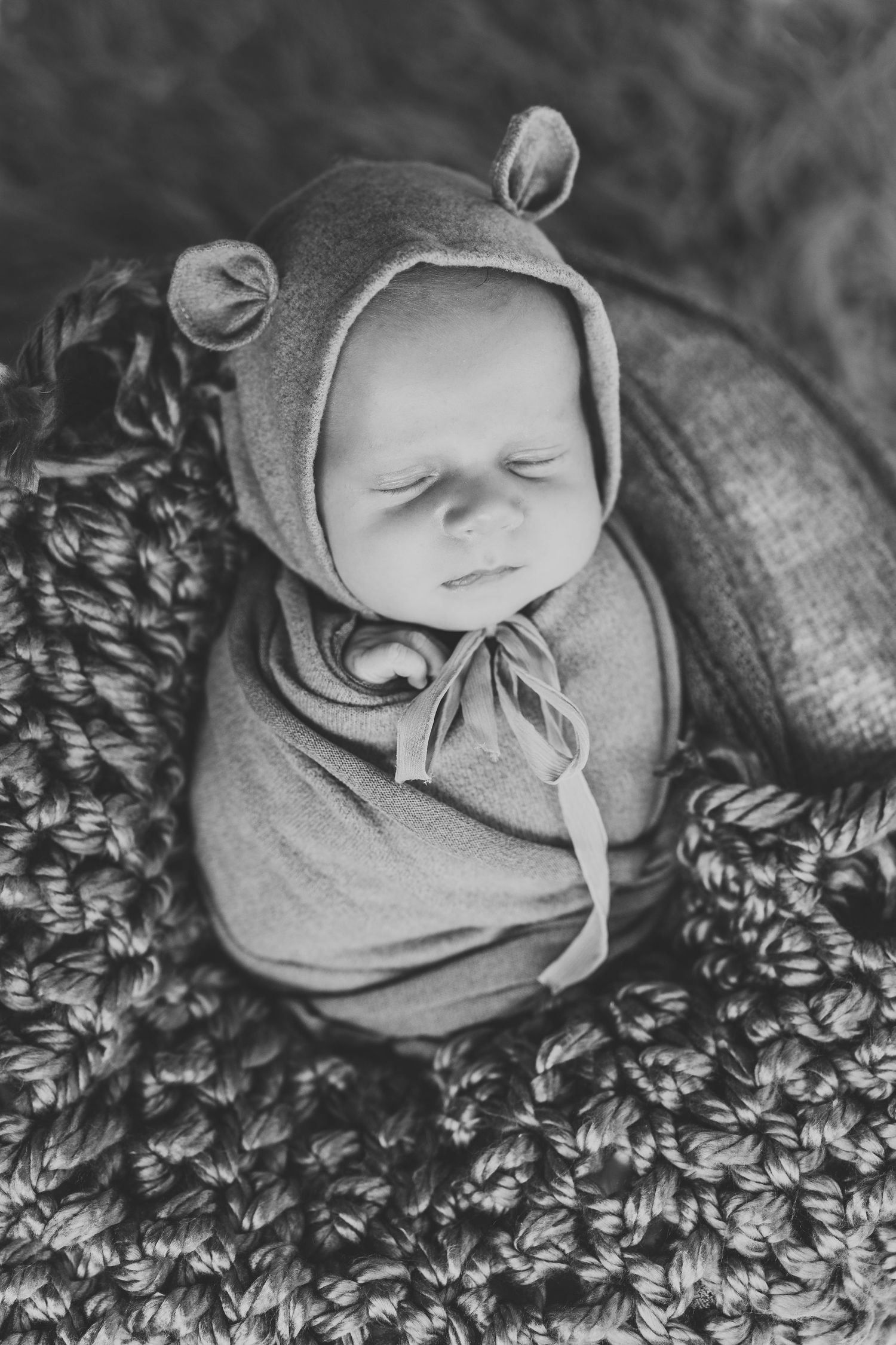 Black and white portrait of sleeping newborn in textured wrap on knit blanket.