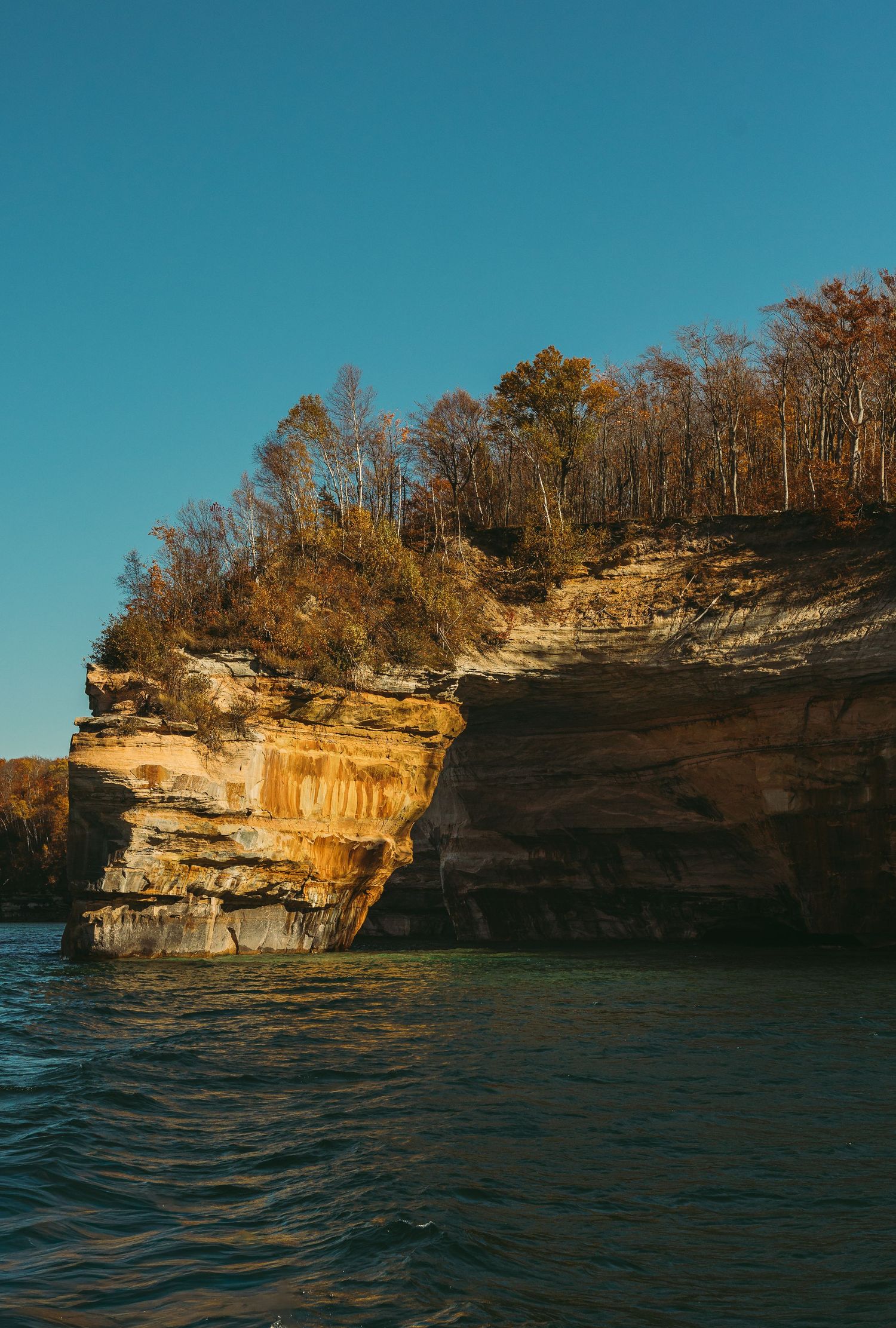 Weathered limestone cliffs meet Lake Superior waters with fall colors decorating the clifftop.