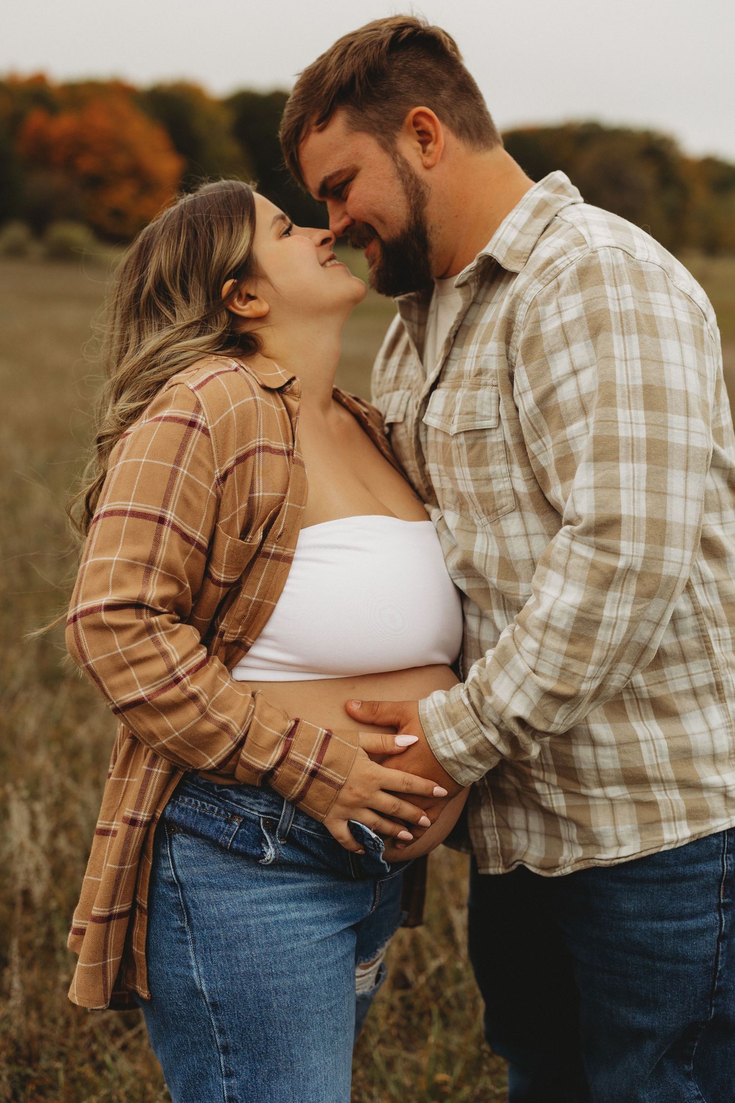 A romantic couple embraces in a golden autumn field wearing coordinating plaid and denim outfits.