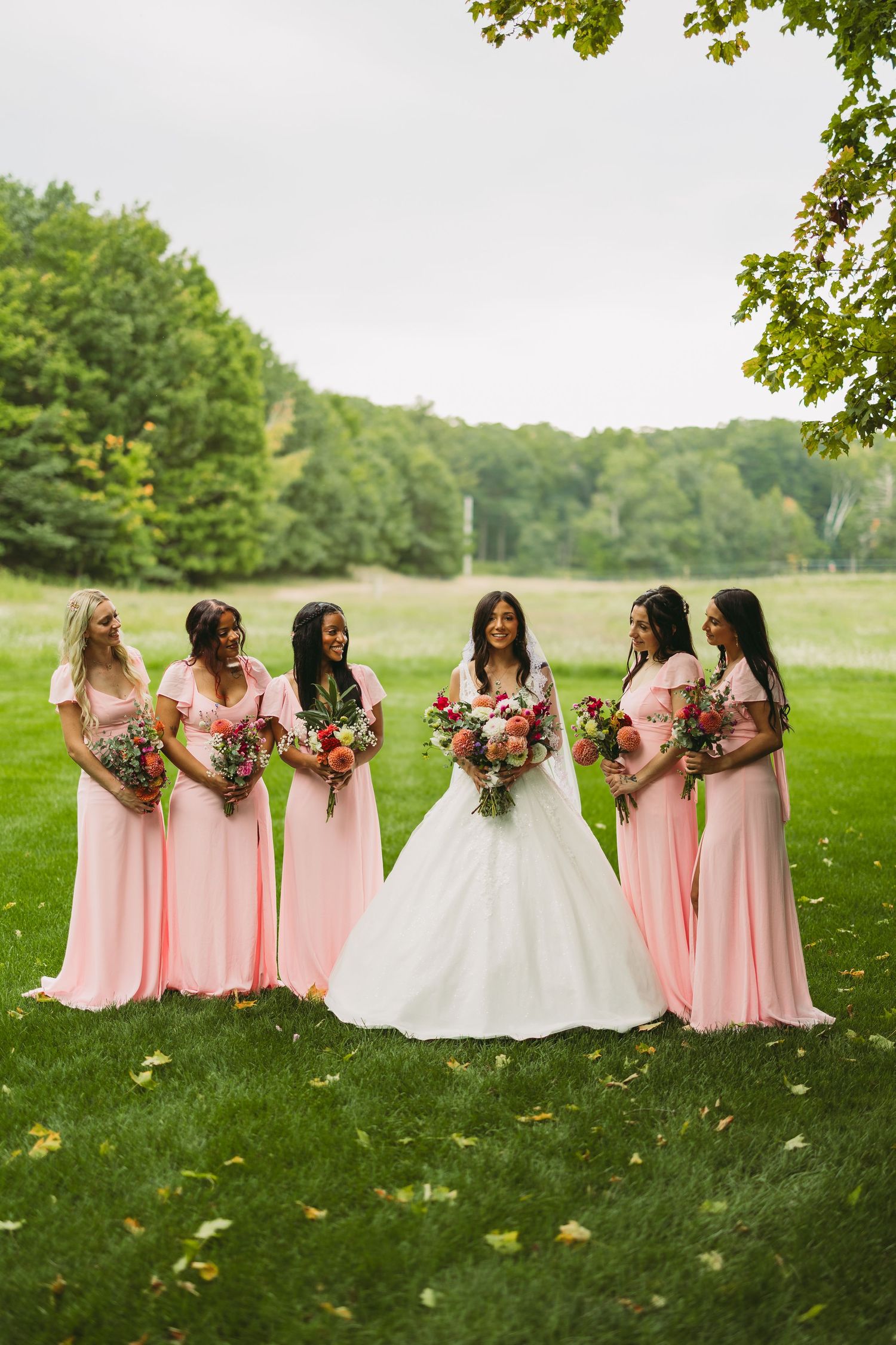 Wedding party poses on grass with bridesmaids in pink dresses and bride in white gown holding bouquets.