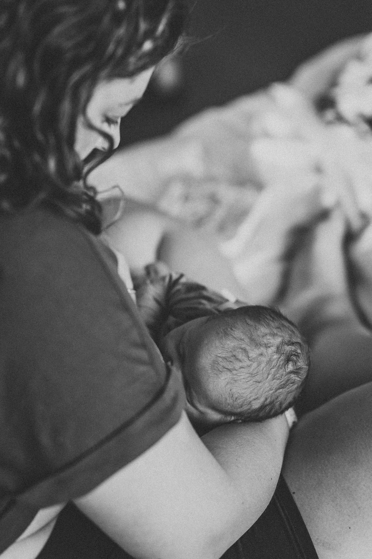Black and white close-up photo showing a tender breastfeeding moment in soft lighting.