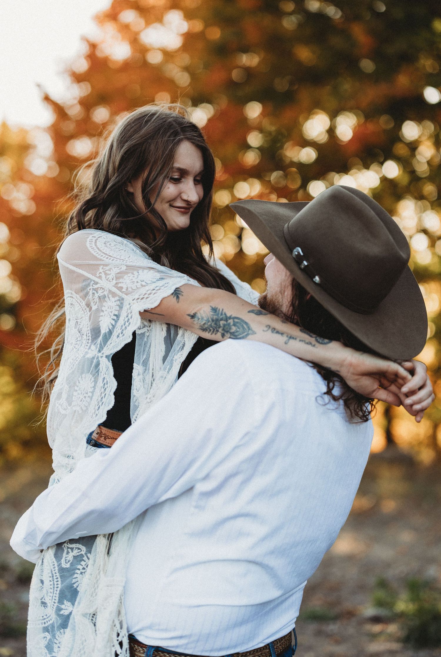 A couple in white and brown attire share an intimate embrace during a golden autumn sunset photo session.