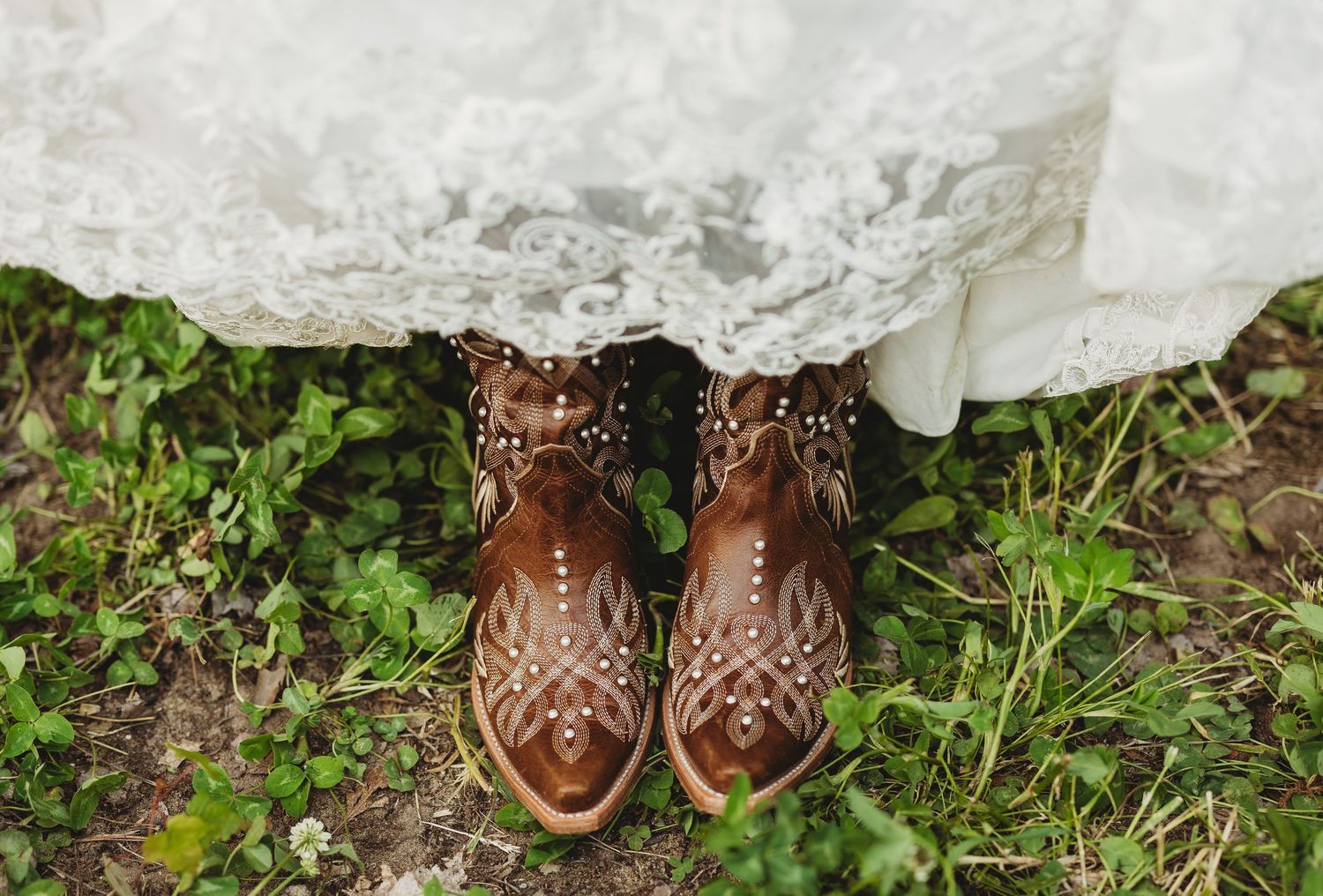 A series of shoes and boots arranged in a row on grass and stone surfaces, showing different footwear styles.