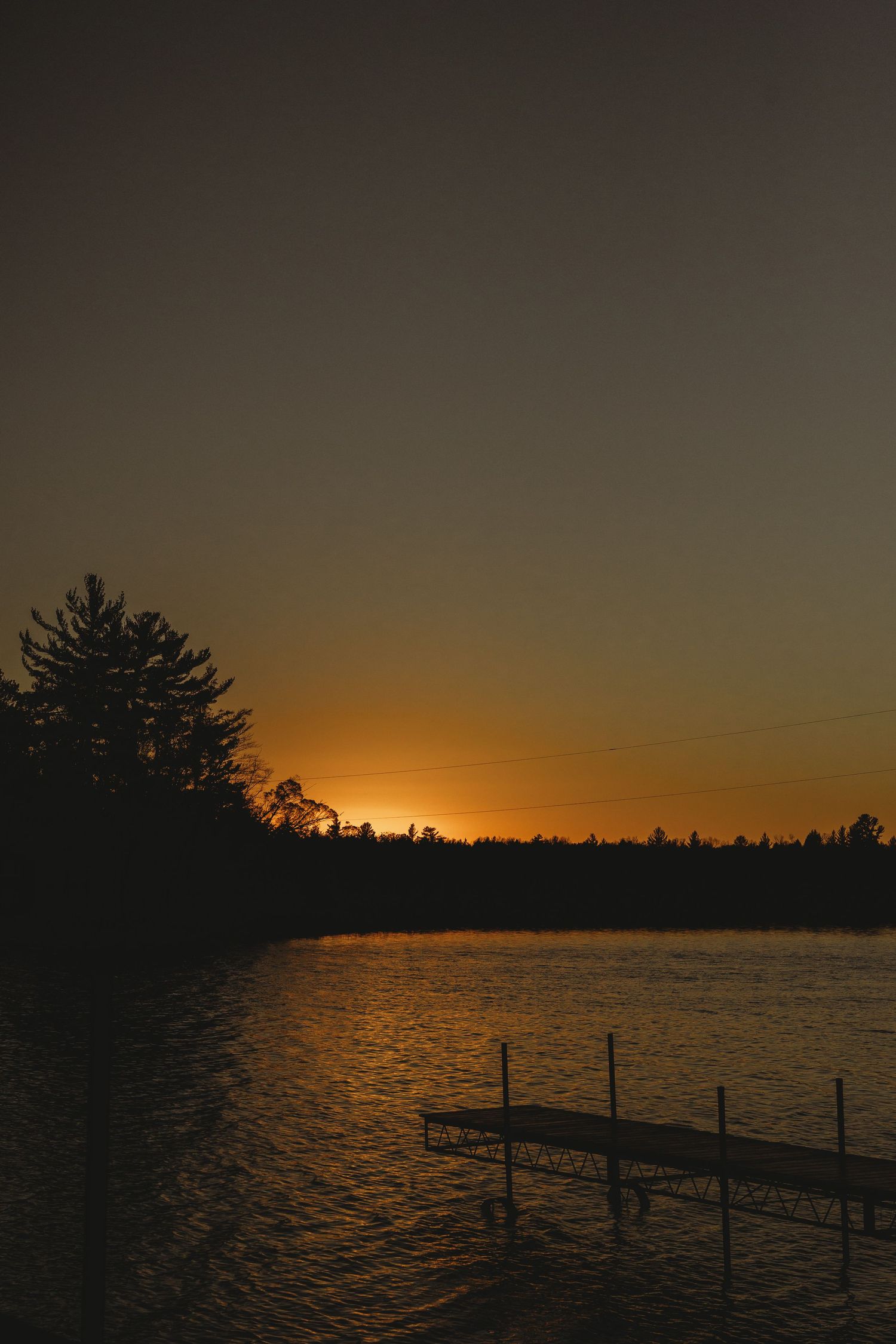 Golden sunset over a lake with silhouetted dock posts in the foreground.