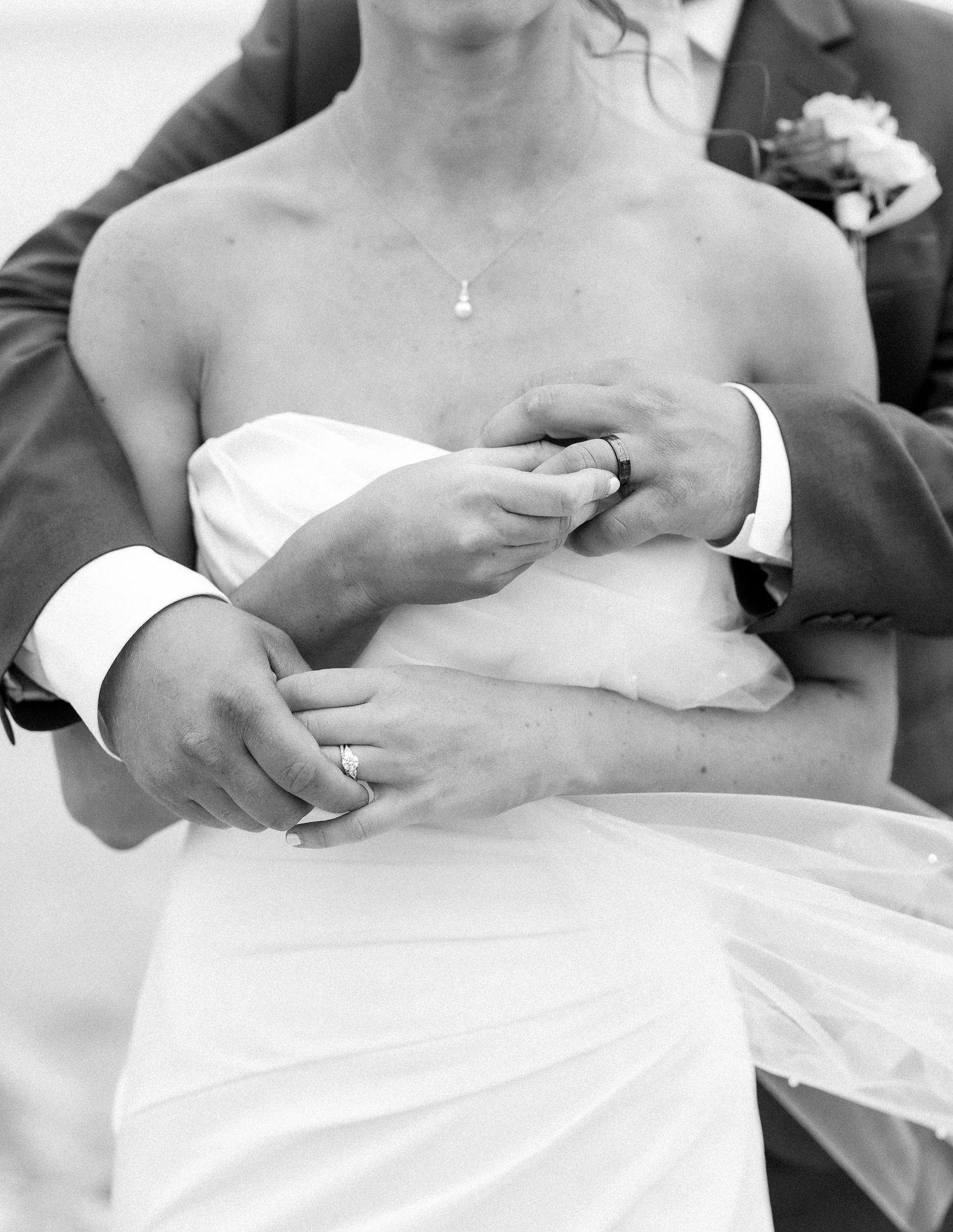 Black and white photo of bride and groom holding hands, showing wedding rings, in an intimate embrace.
