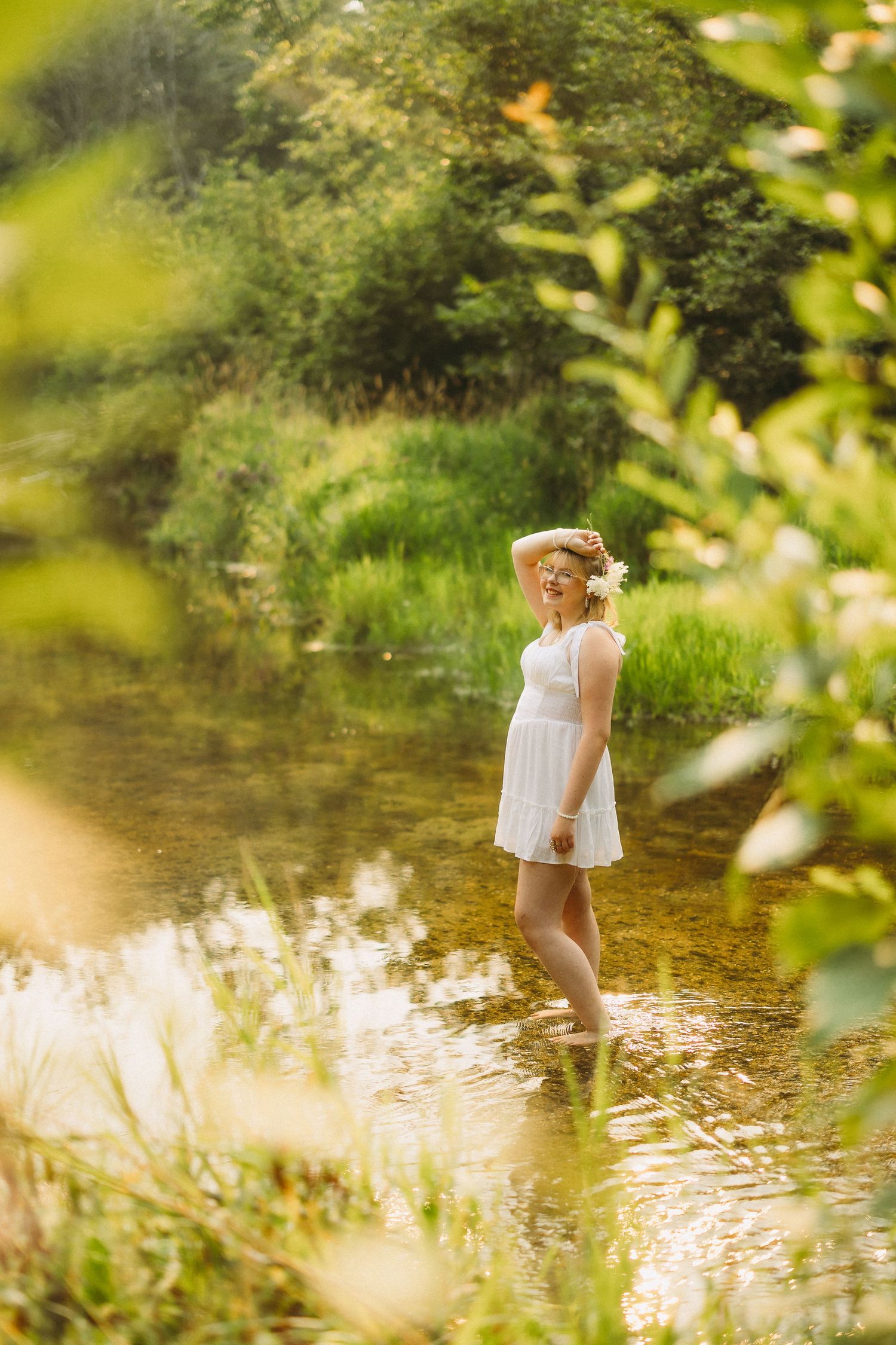 Person exploring shallow stream water in natural setting with golden sunlight filtering through trees.
