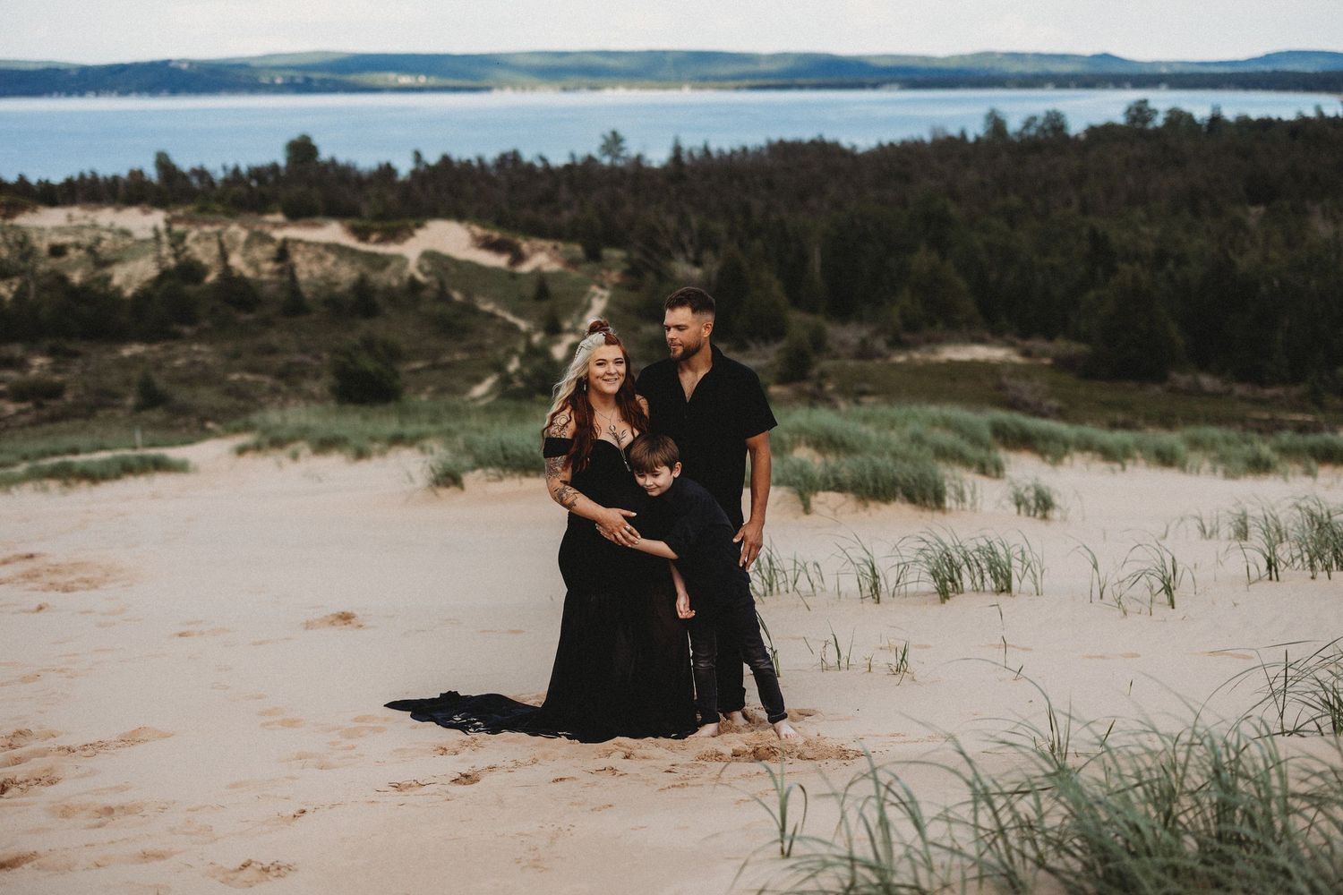 A couple shares a romantic moment on a sandy beach with coastal grass and dunes in the background.