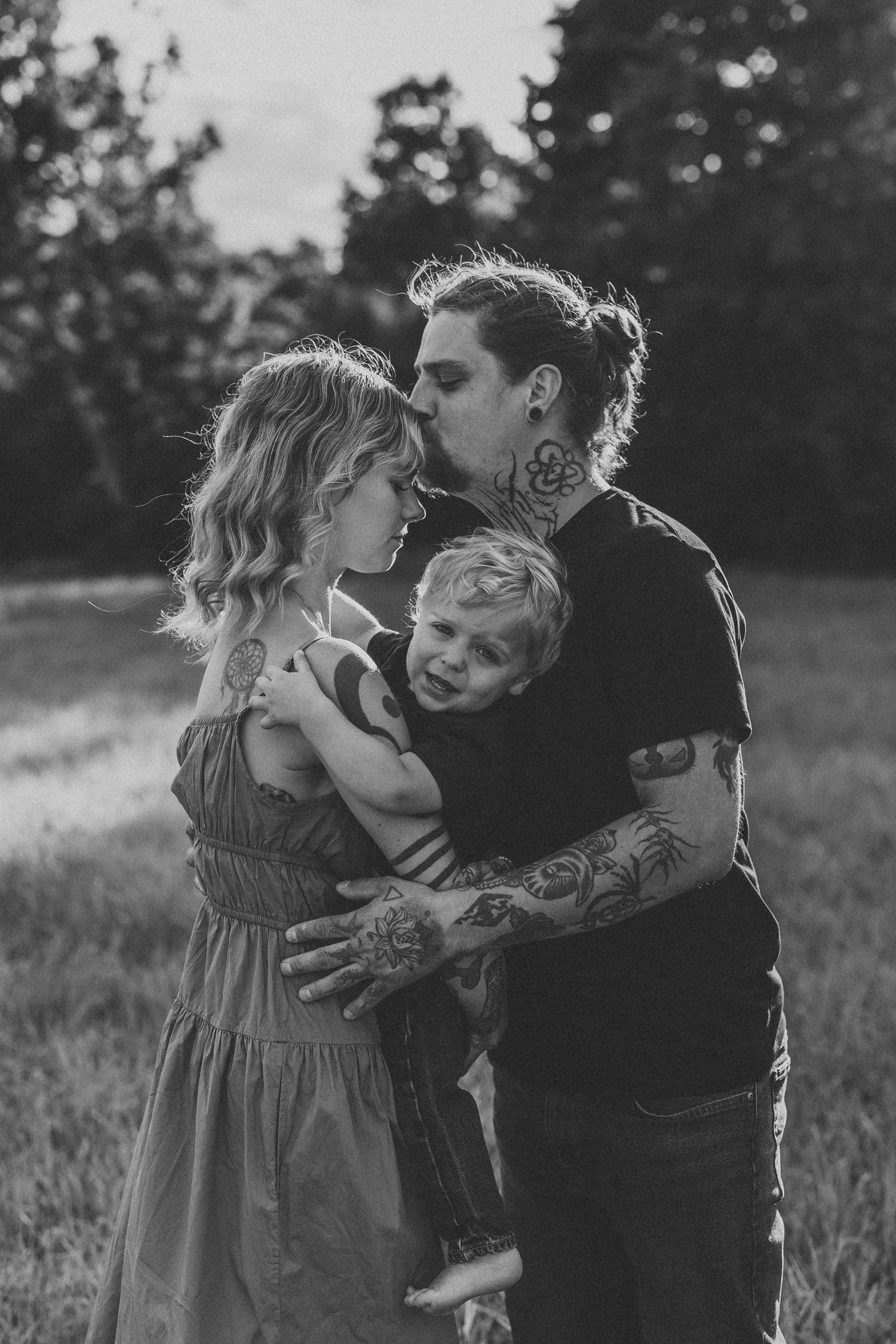 An intimate black and white family portrait showing tender moments in a natural outdoor setting.