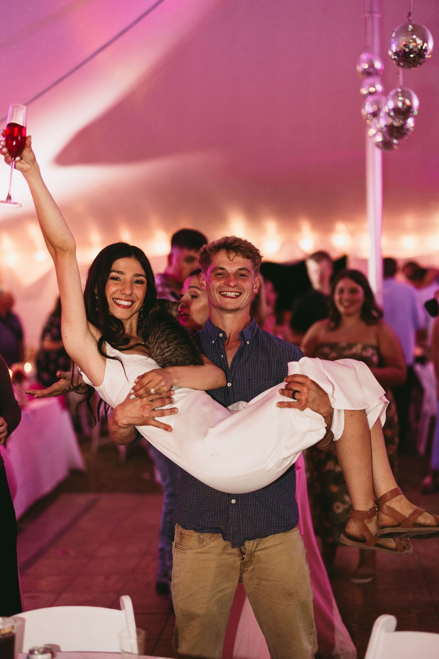 Wedding couple dances joyfully under pink lighting at their reception celebration.