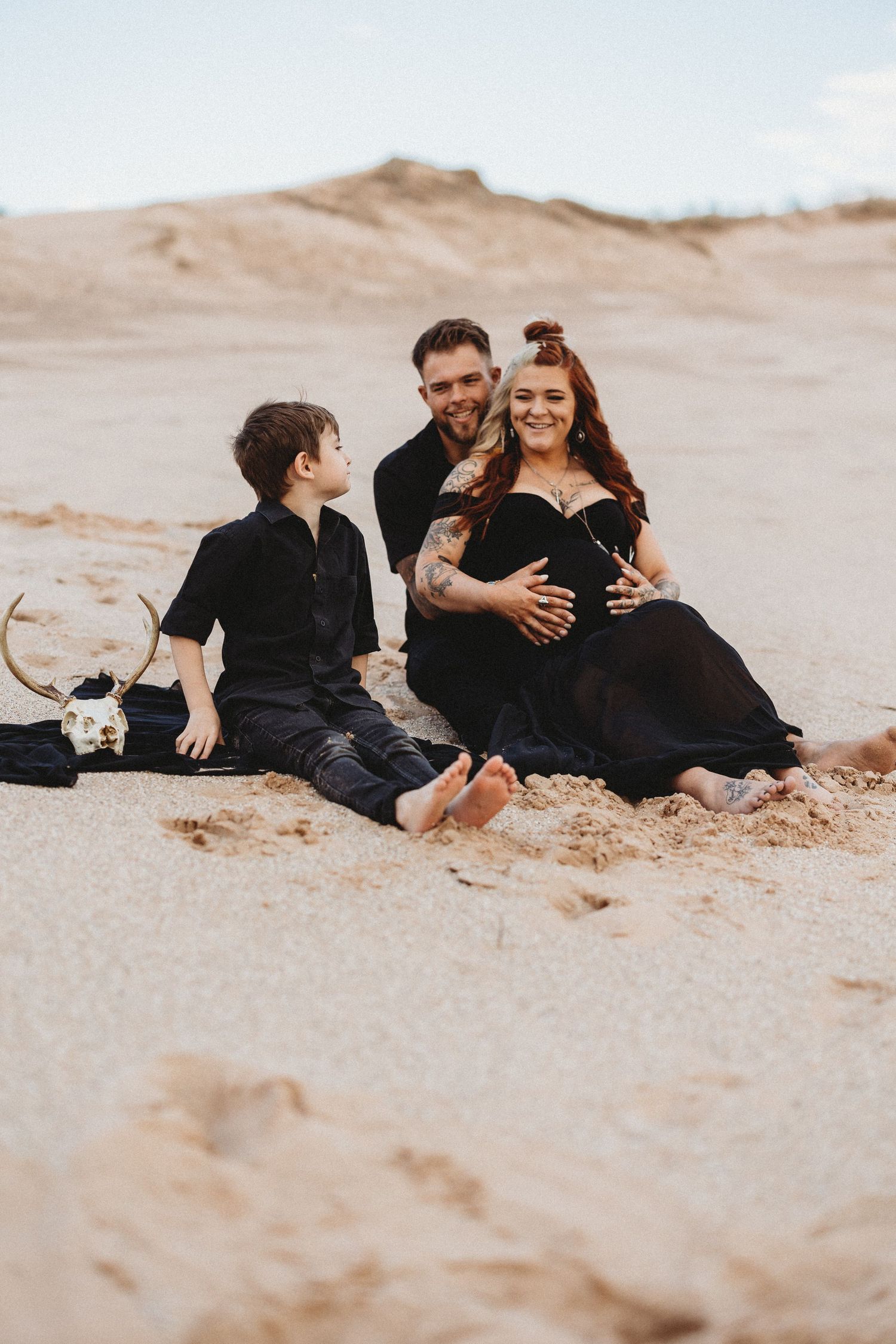 Family members in black clothing relax together on a sandy beach during an outdoor photoshoot.