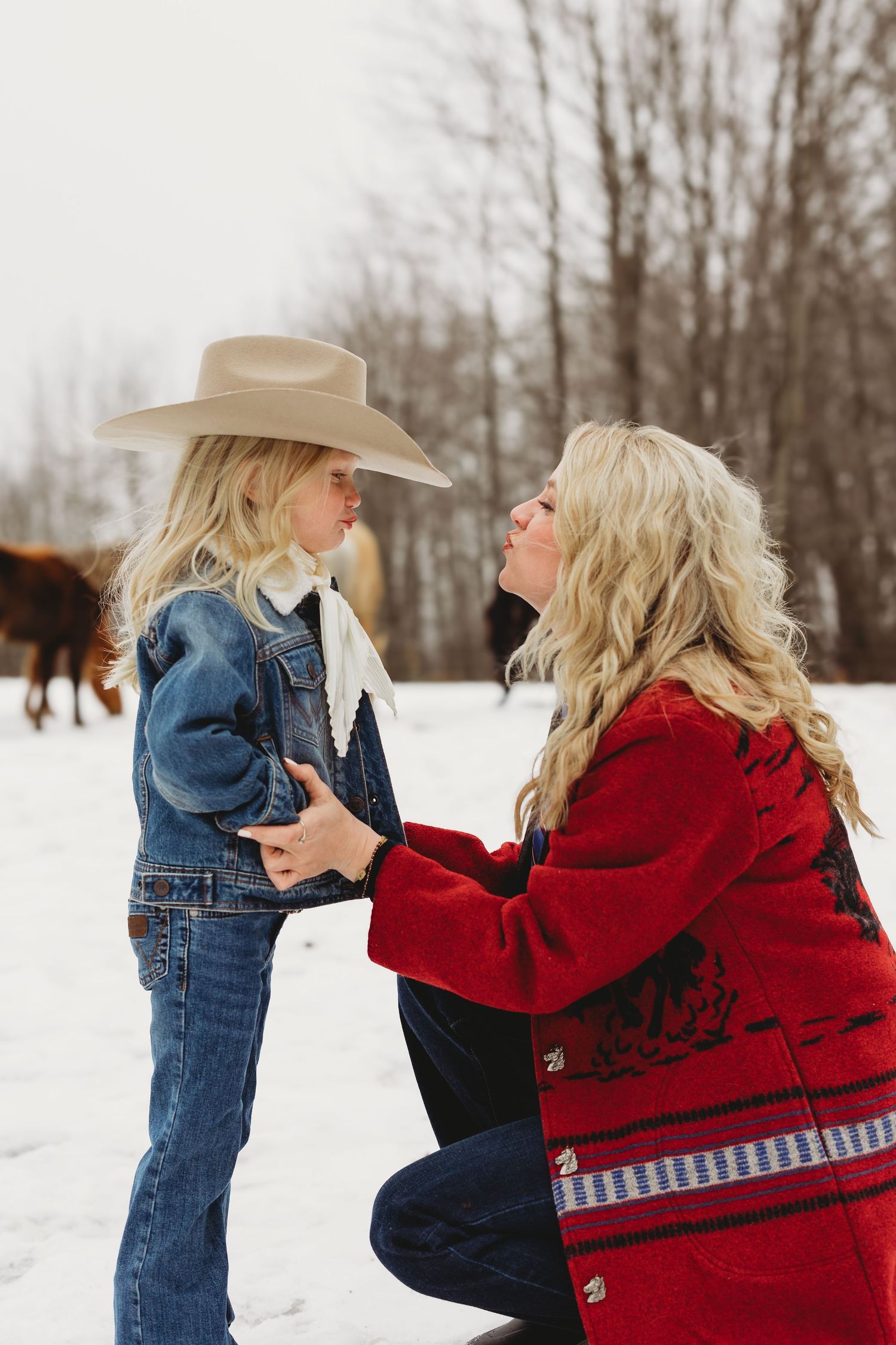 Two people playfully interacting in a snowy winter landscape wearing denim and red clothing.