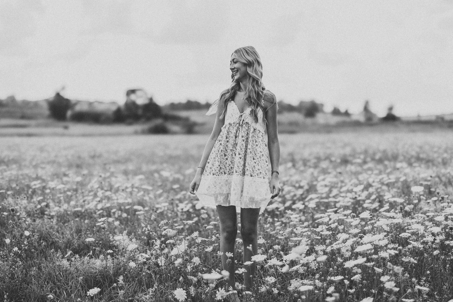 A person in a flowy dress stands in a field of white wildflowers on a sunny summer day.