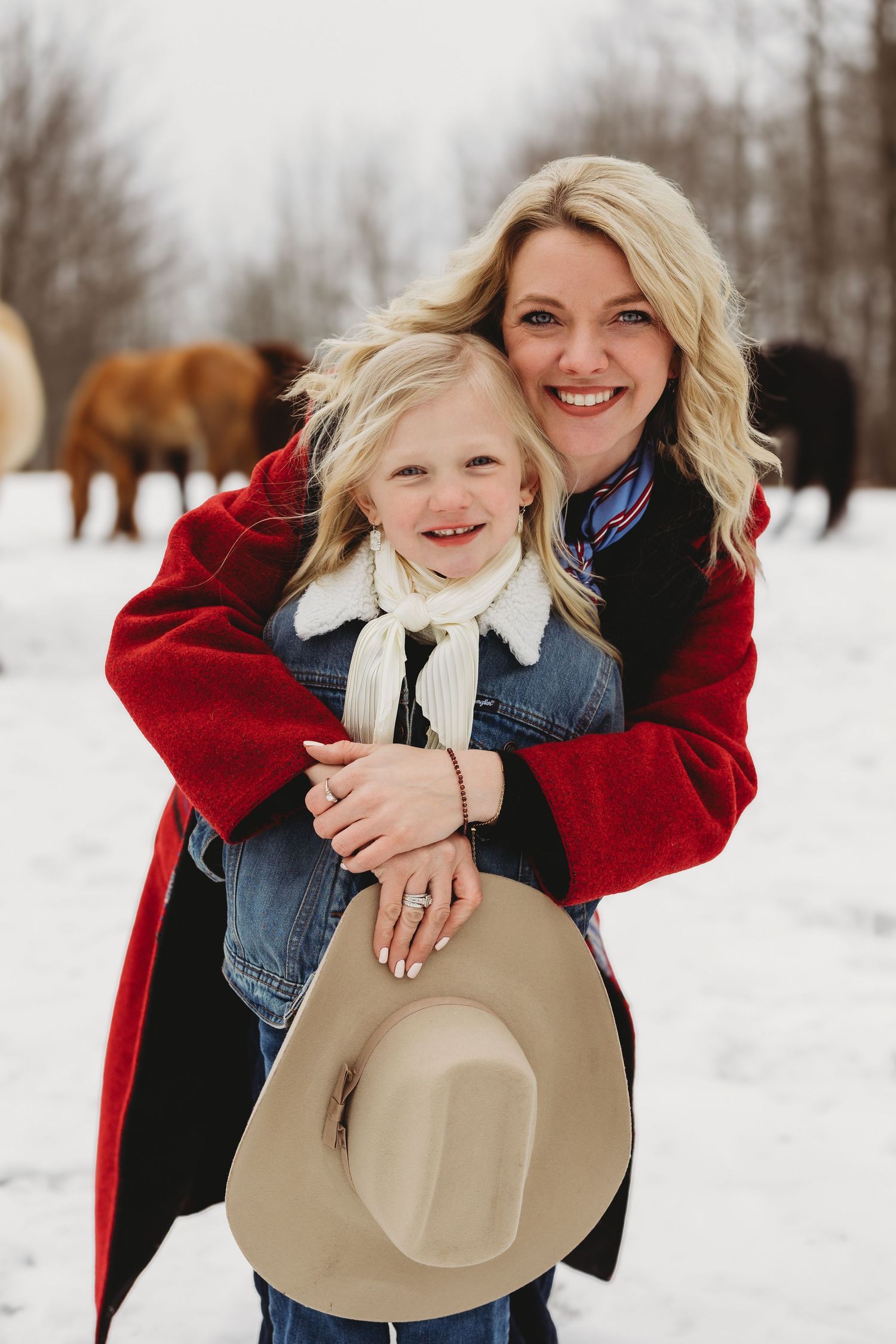 Mother and daughter share joyful moments together in a snowy winter setting wearing red coats and denim.