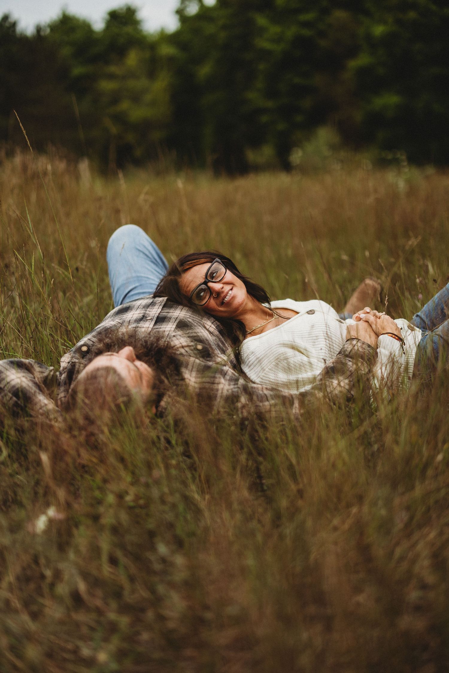 Couple lying together in tall grass field during golden hour.