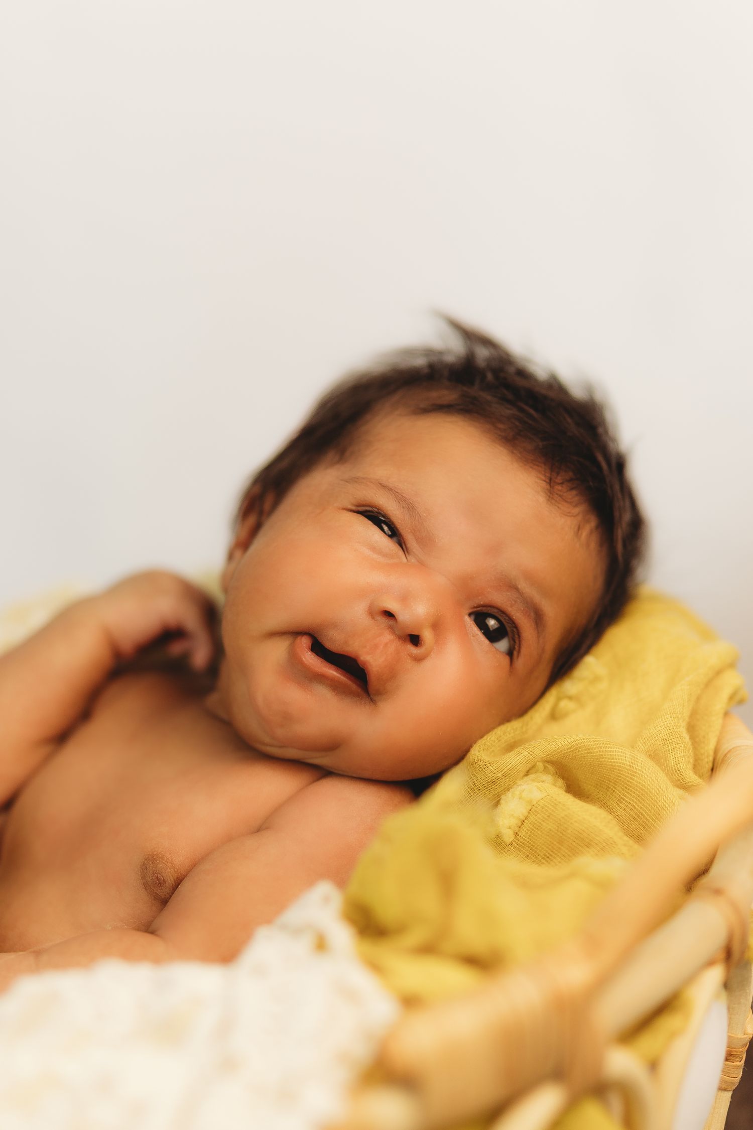 Adorable newborn baby smiling while resting in a basket with yellow blanket.