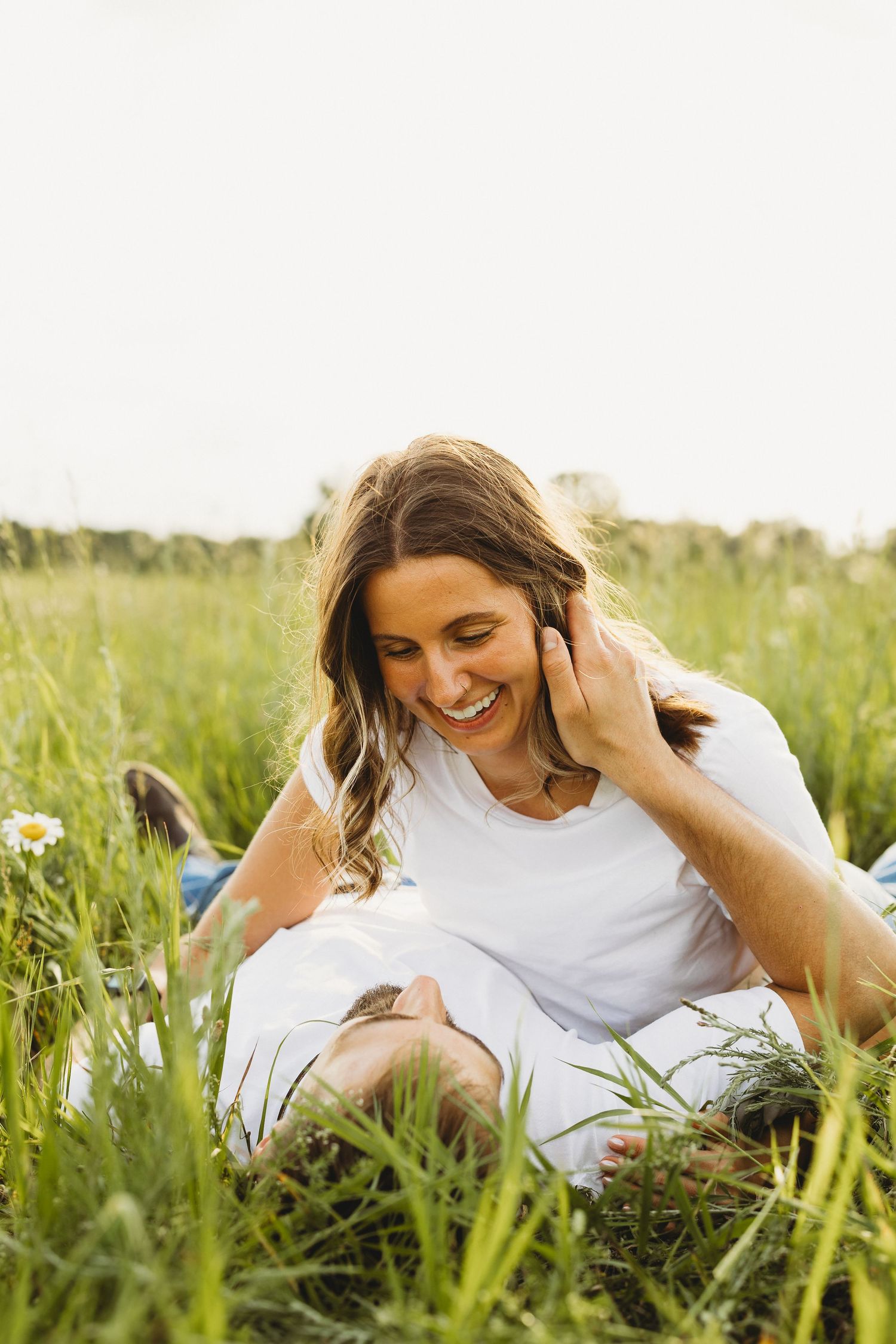 Happy woman laughing while sitting in tall grass field, enjoying a romantic outdoor moment with her partner.