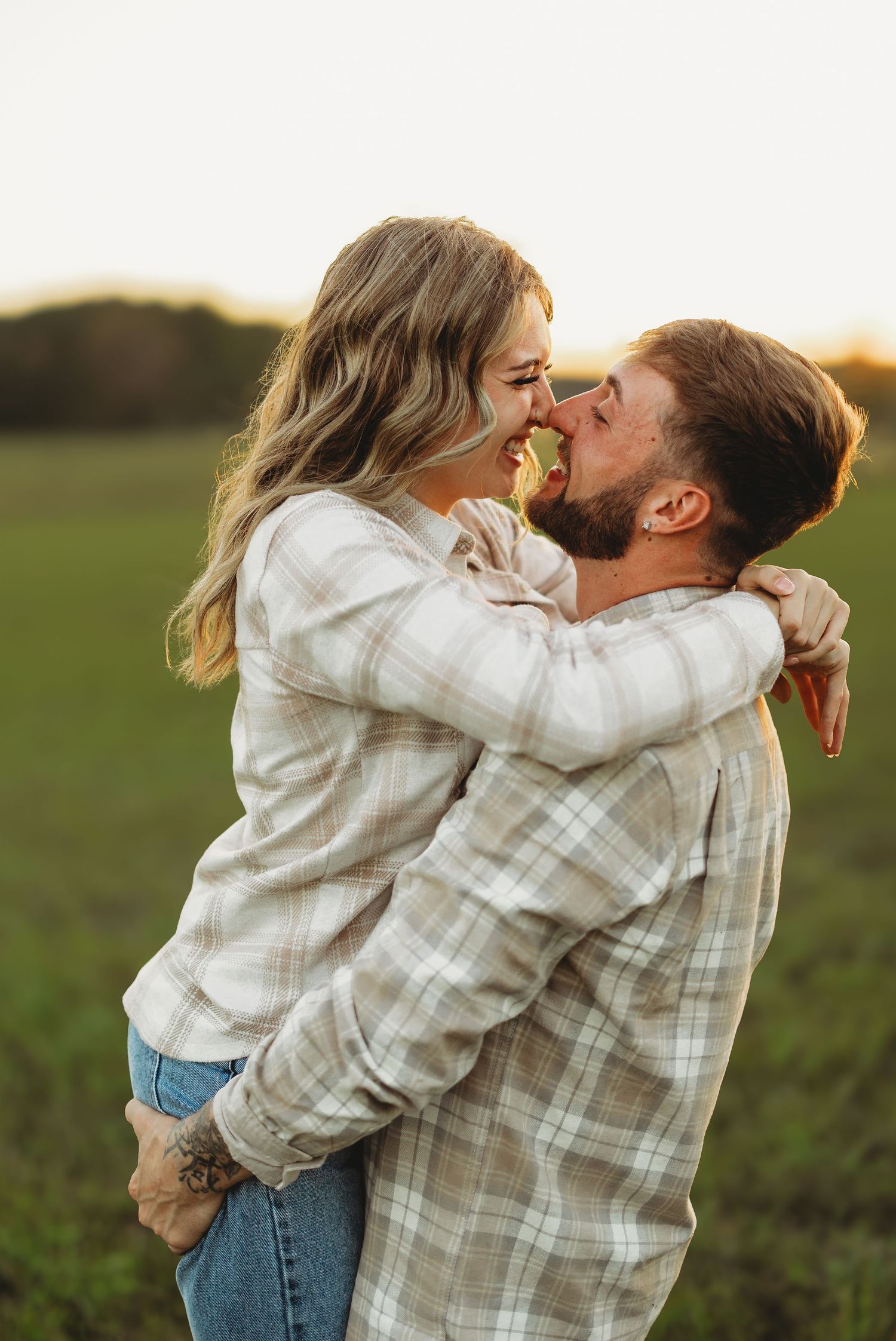 Romantic couple embracing in a field at sunset wearing plaid and white shirts.