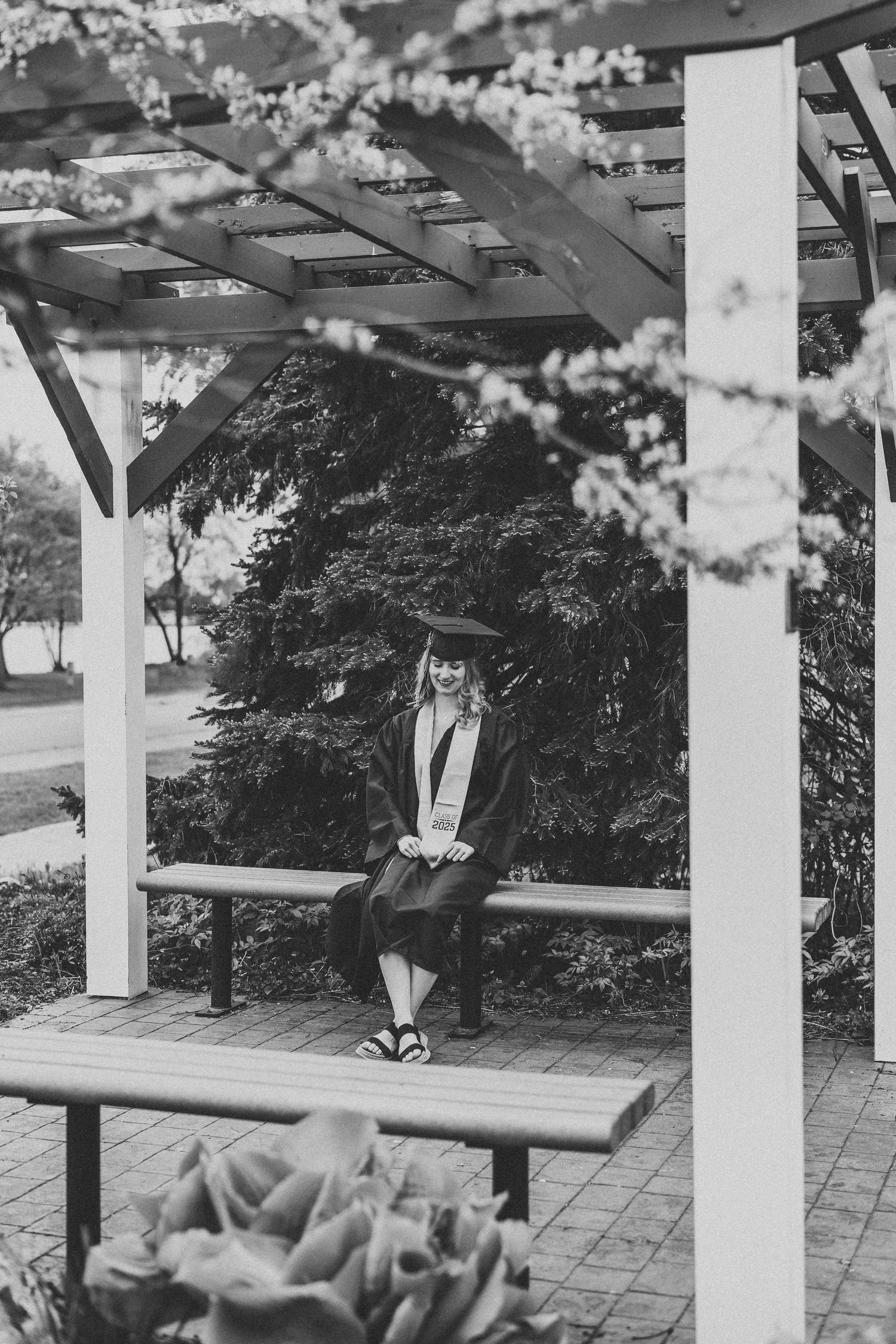 Black and white photo of a graduate sitting on a bench under an outdoor pergola.