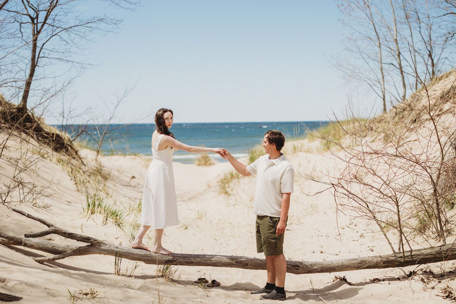 A romantic beach photoshoot sequence showing a couple walking along sandy dunes with bare trees in winter.
