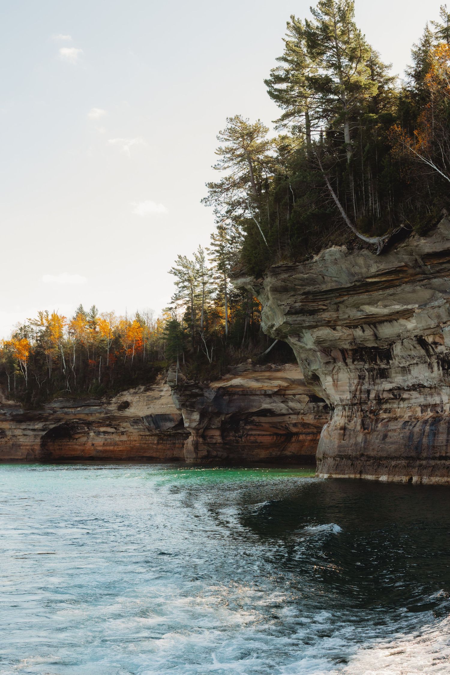 Dramatic limestone cliffs rise above turquoise waters along a scenic shoreline during autumn.